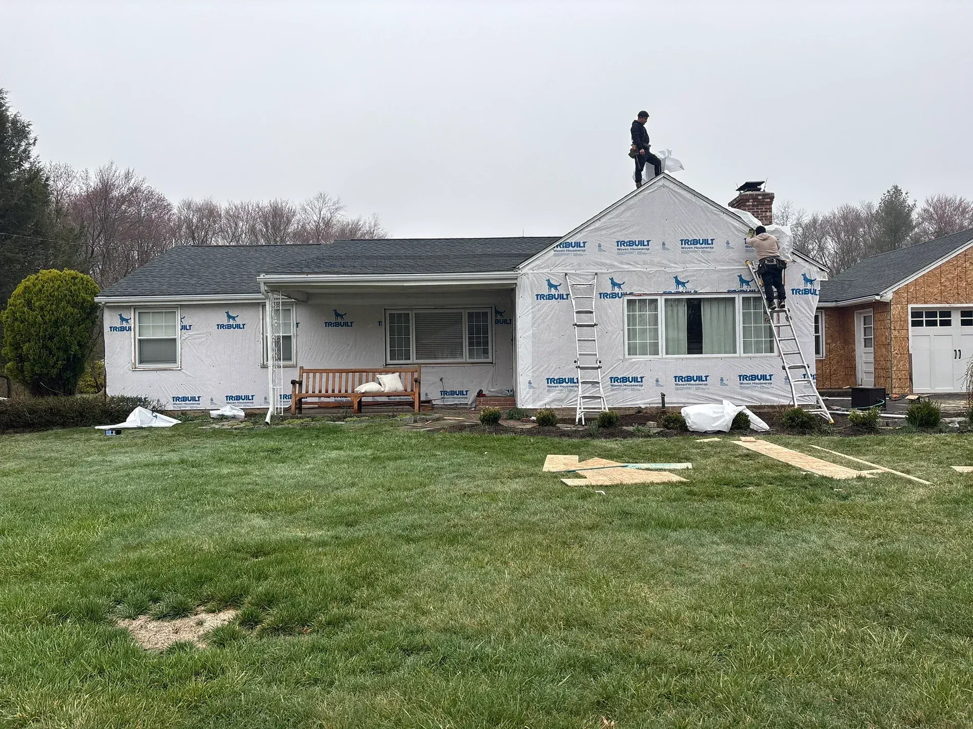 Damaged house roof with workers repairing shingles in a suburban yard