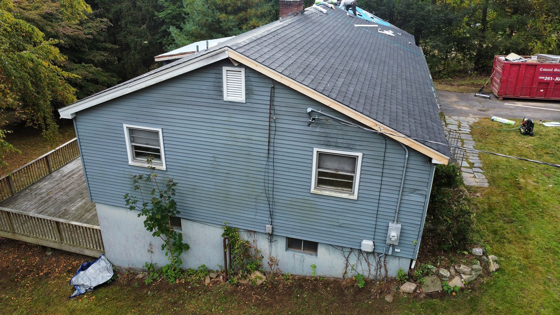 Blue-sided house with white trim and sloped roof, viewed from above in a wooded yard