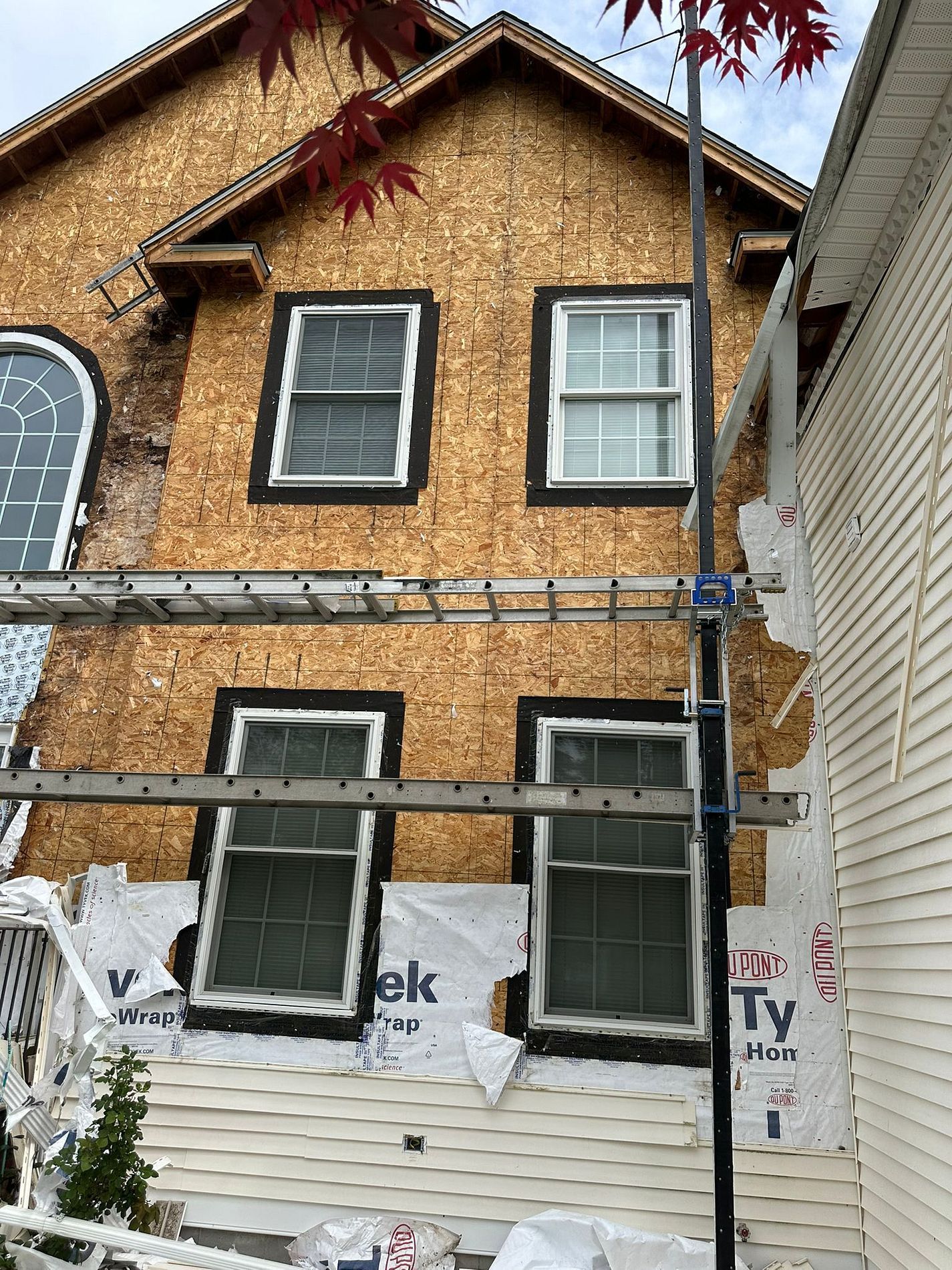Partially renovated house facade with exposed sheathing, white lower siding, and scaffolding in front