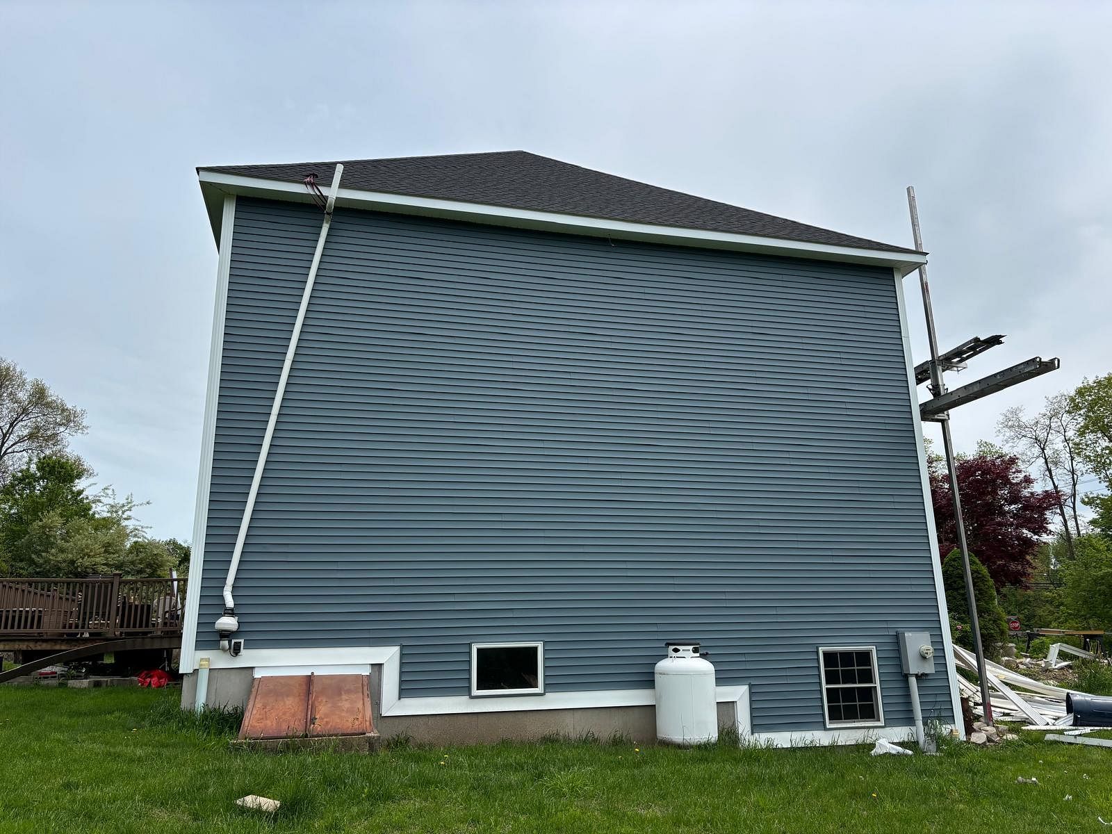 Side view of a blue-gray house with white trim, showing foundation damage and debris near the base.