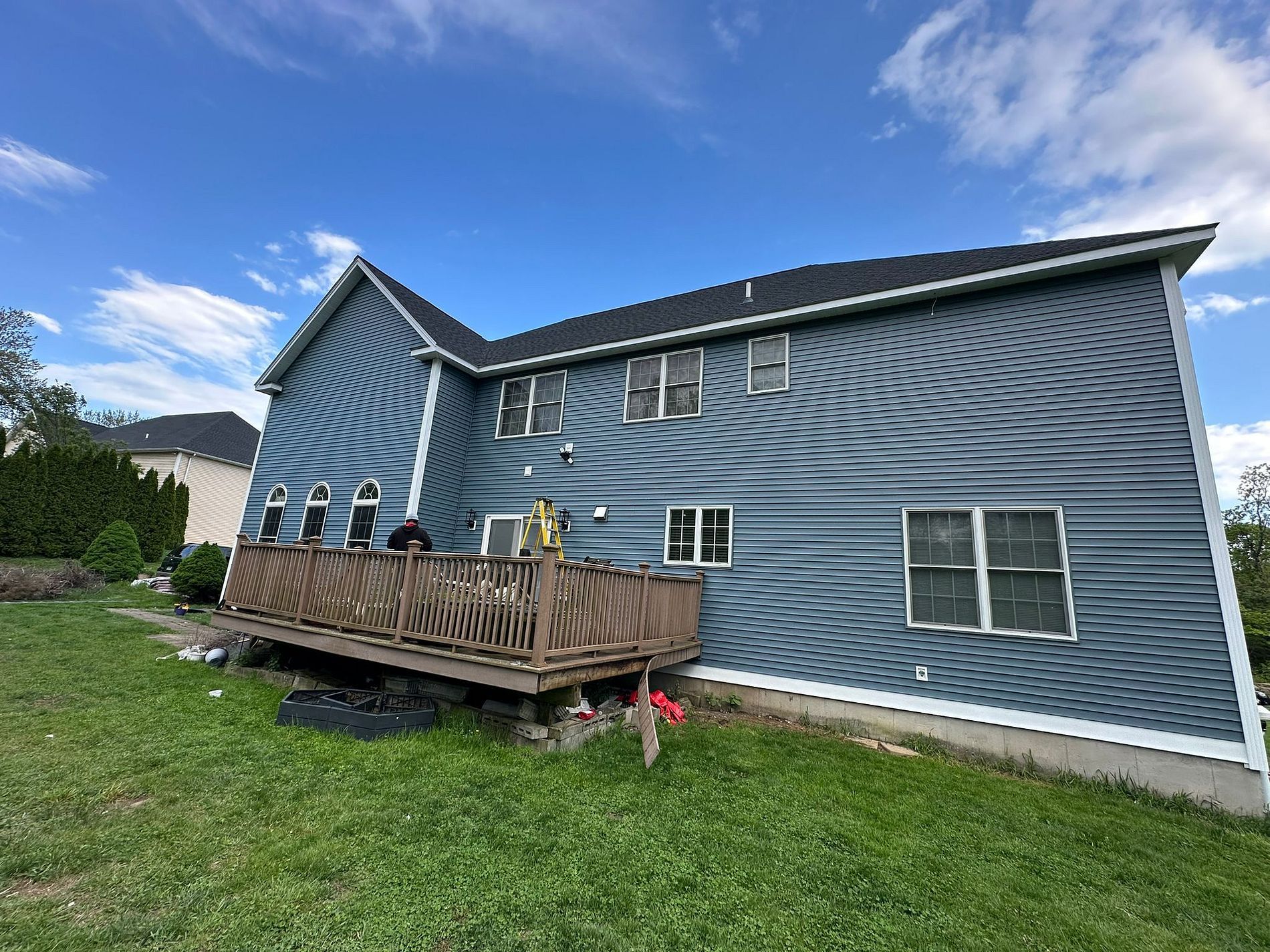 Blue house with wavy siding, small wooden deck, and grassy yard under a cloudy sky.
