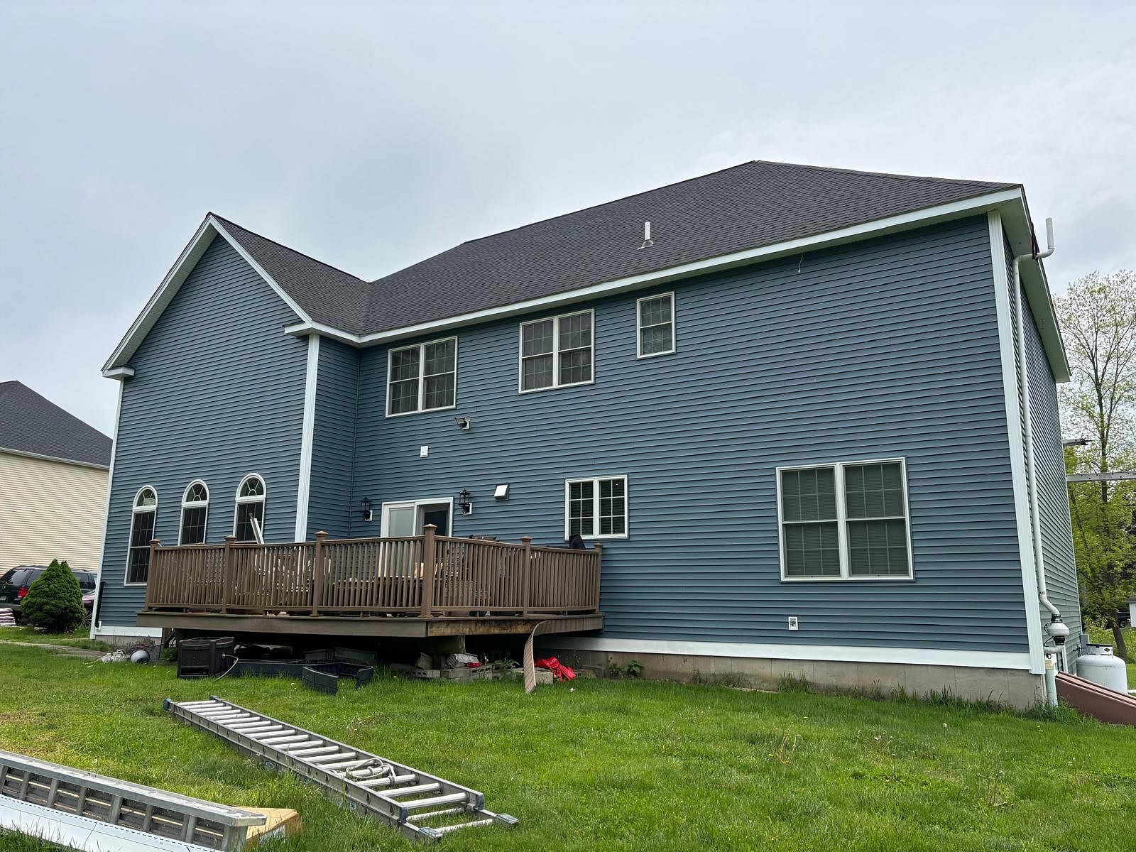 Blue two-story house with a wooden deck and sloped roof in a suburban yard