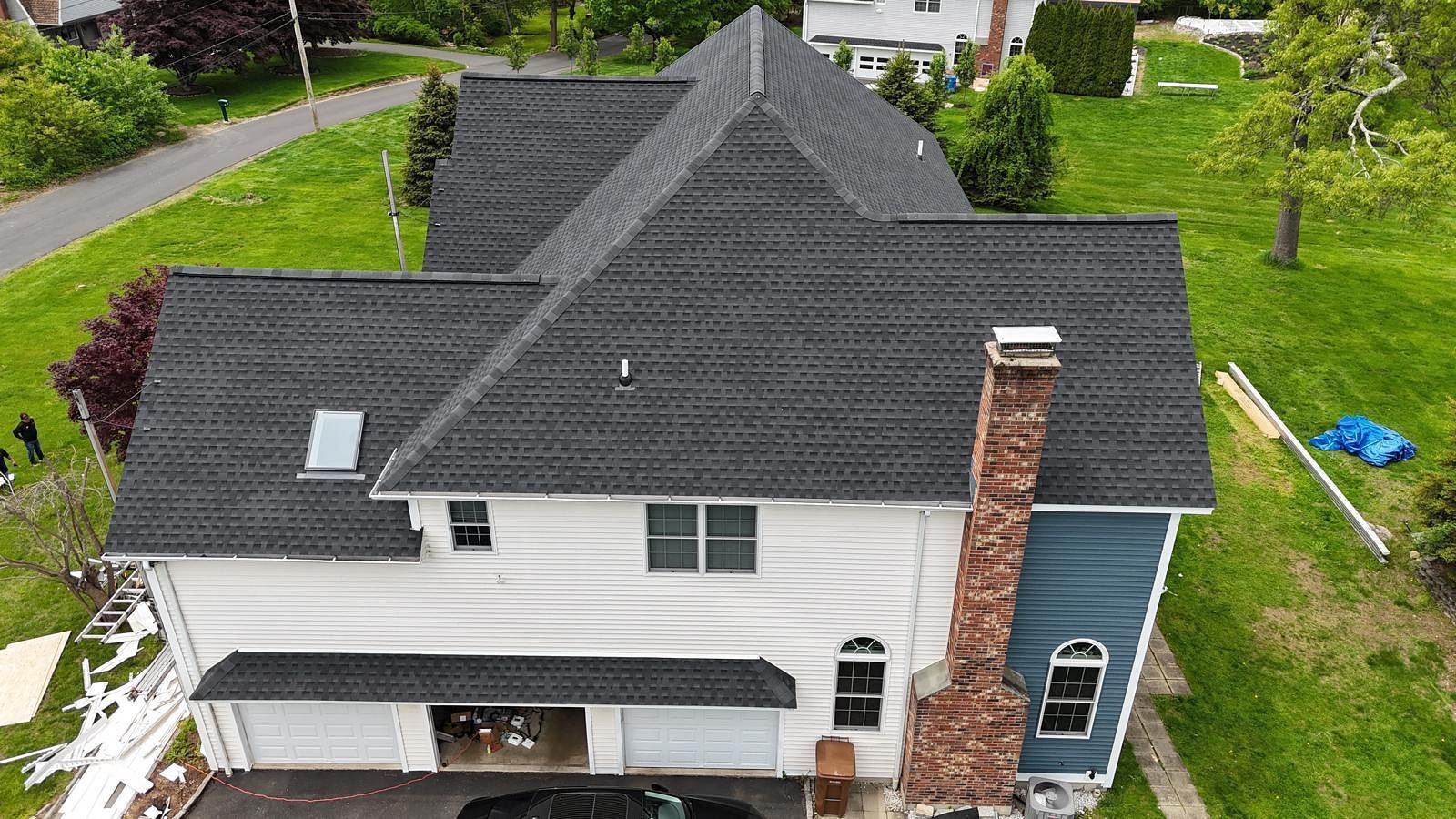 Aerial view of a white house with a dark roof, brick chimney, and green yard in a residential neighborhood