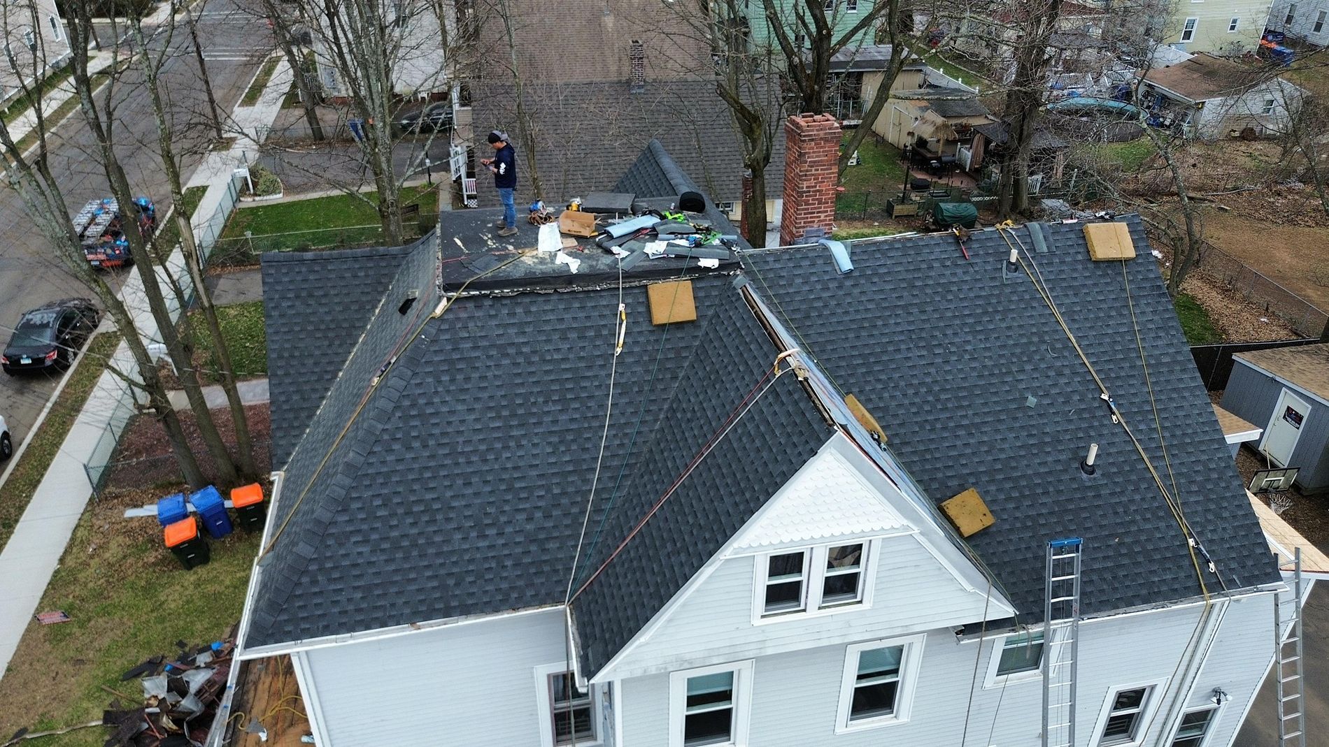 Aerial view of a white house with dark roof shingles and roof repair materials near the top ridge.