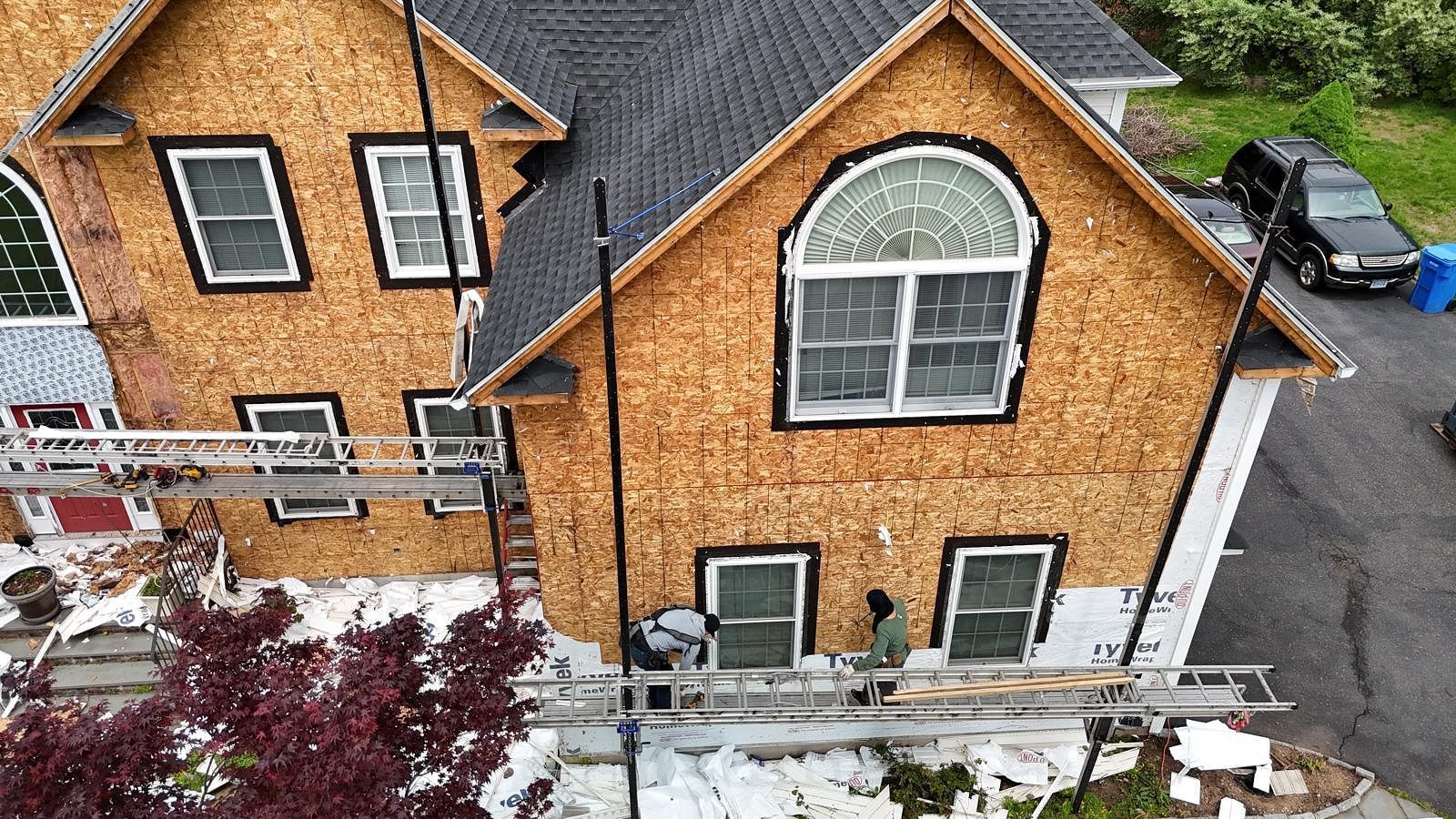 Snow-covered brick house with arched window, white porch railing, and driveway beside it