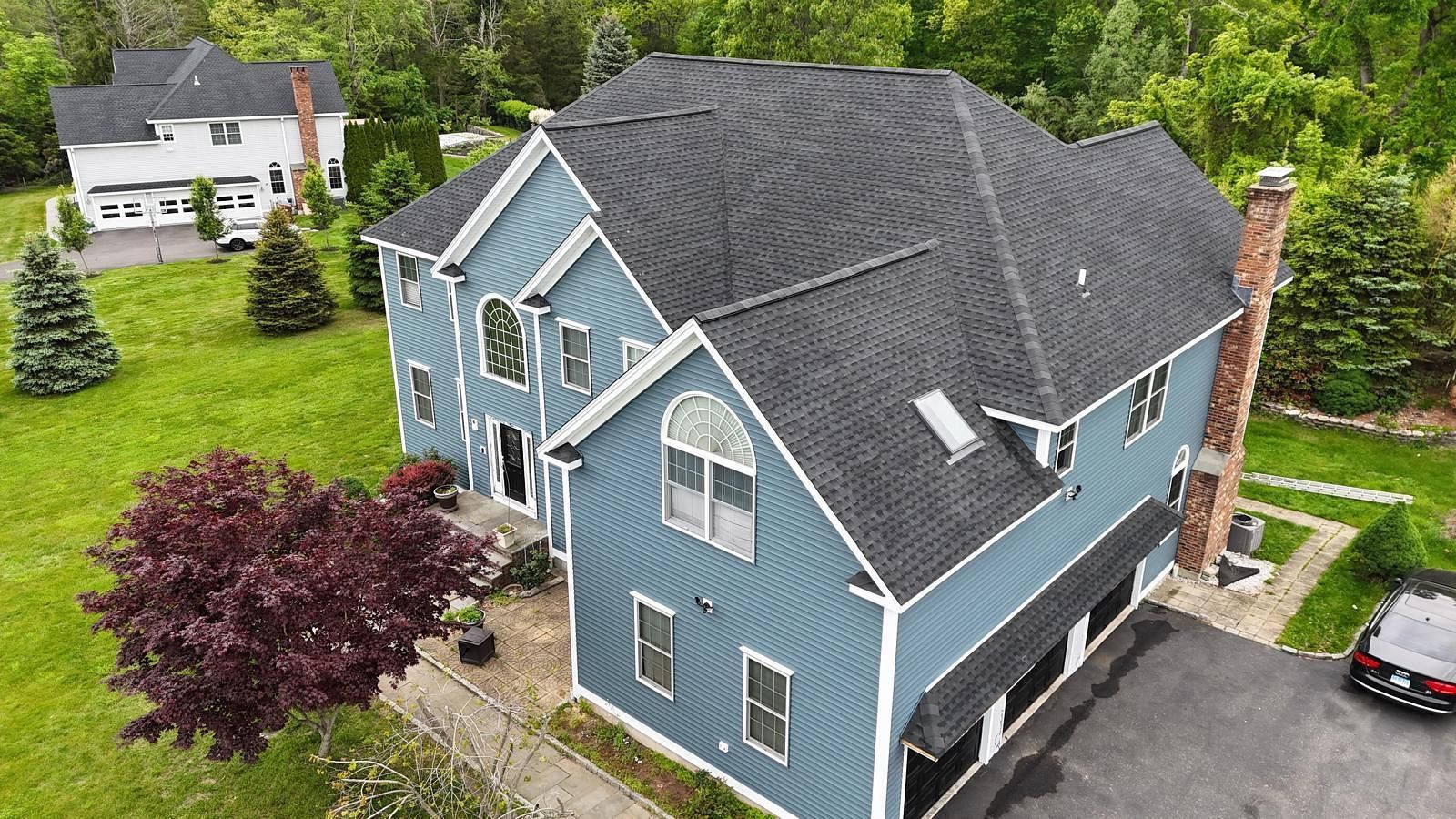 Aerial view of a blue house with a dark roof, surrounded by green trees and a driveway.