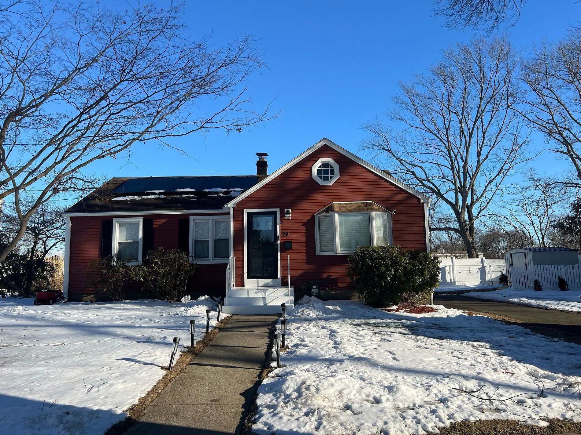 Red house with snow-covered yard and walkway under a clear blue sky