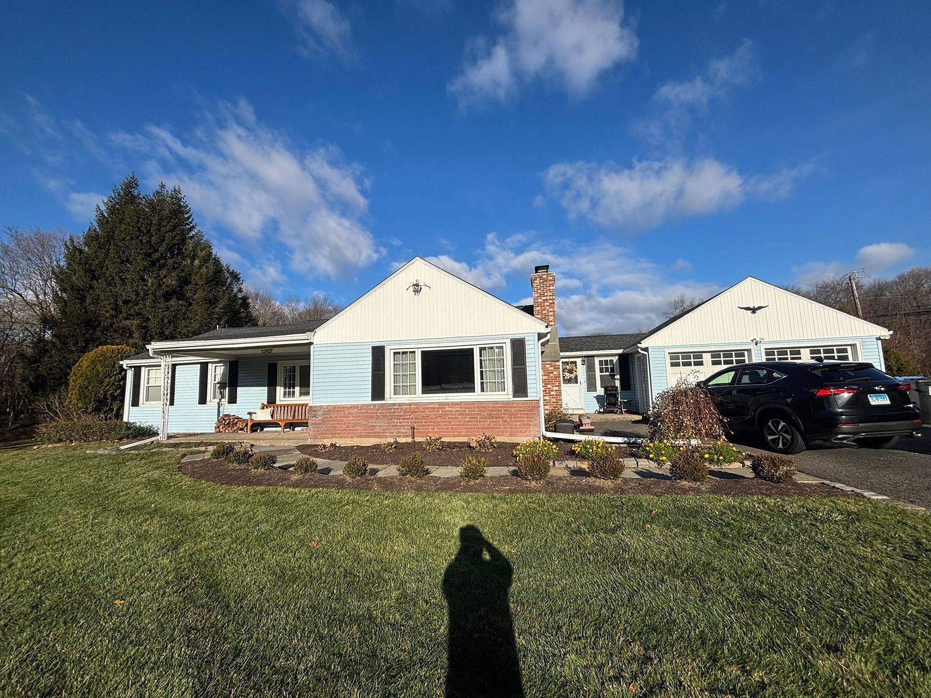 Single-story white house with a brick porch, black car in driveway, under a blue sky