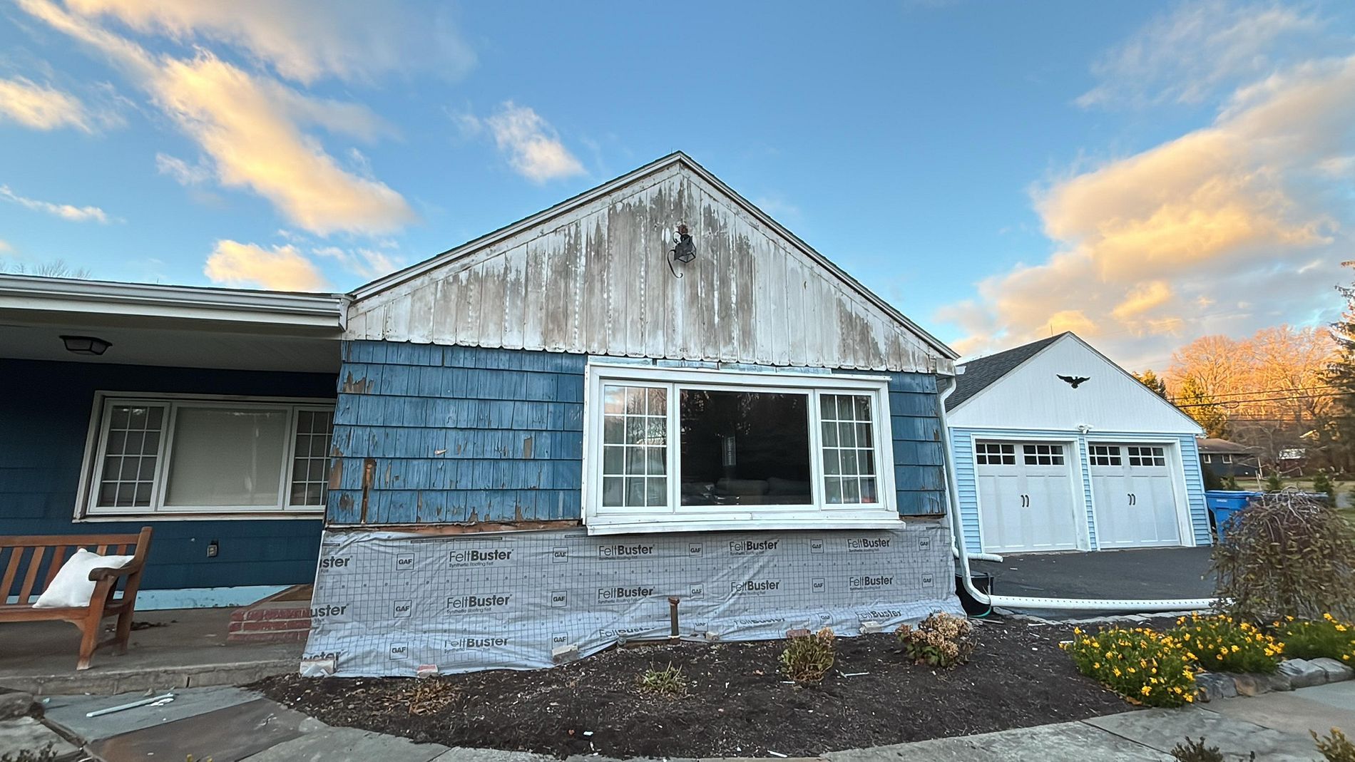 Weathered white house with blue trim and attached garage under a cloudy sunset sky