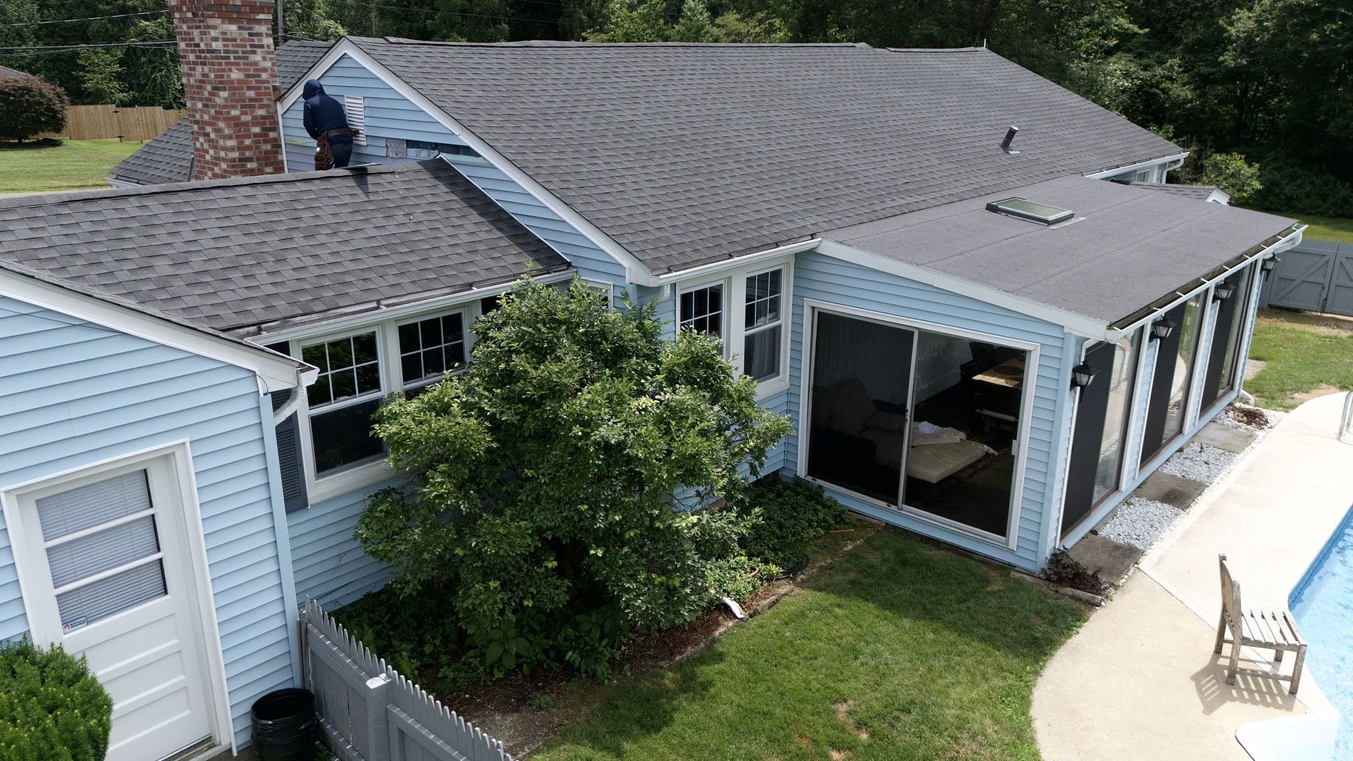 Aerial view of a blue house with a screened porch, gray roof, and a tree in the front yard.
