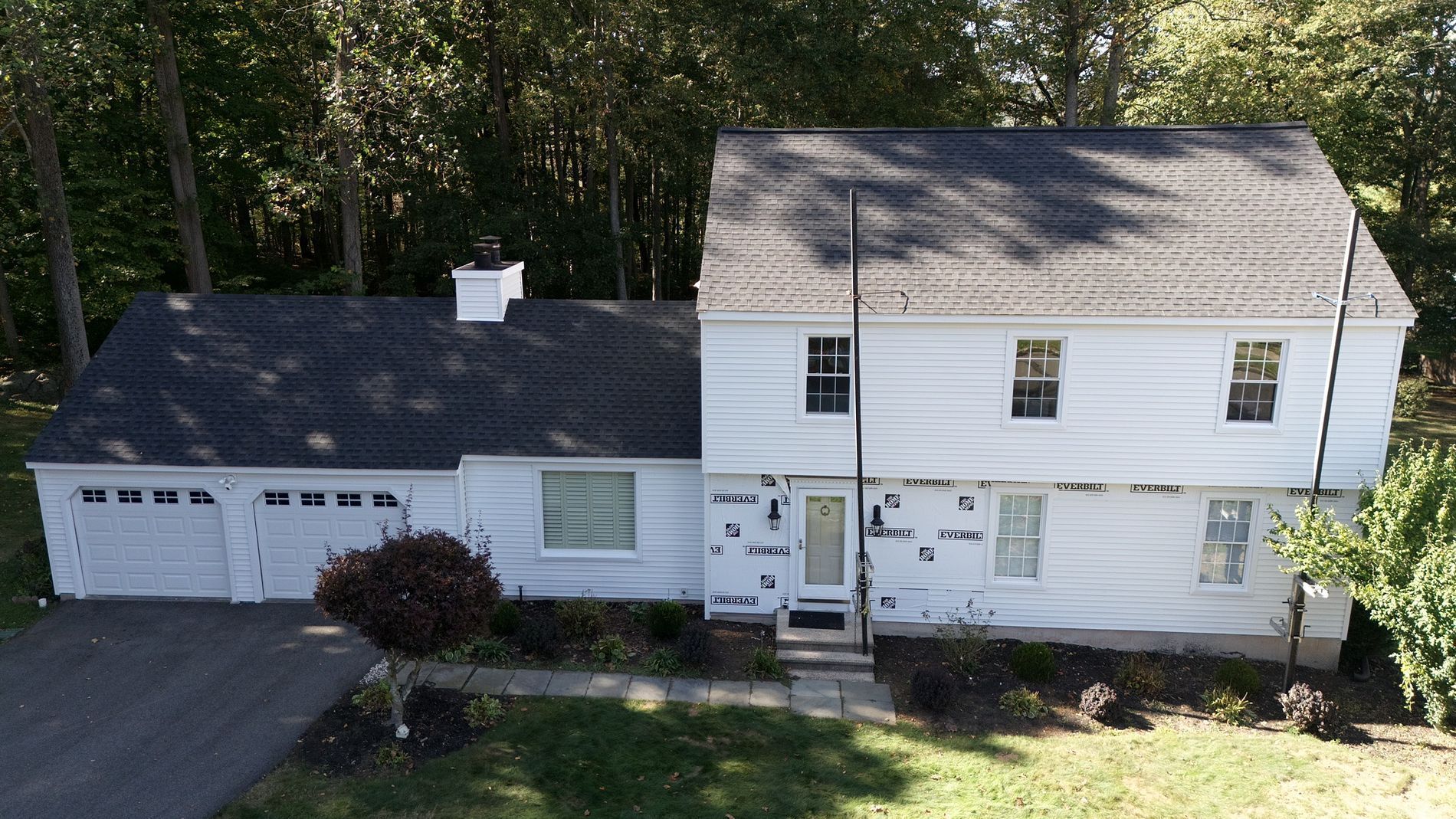Aerial view of a white two-story house with an attached garage, surrounded by trees and a driveway.