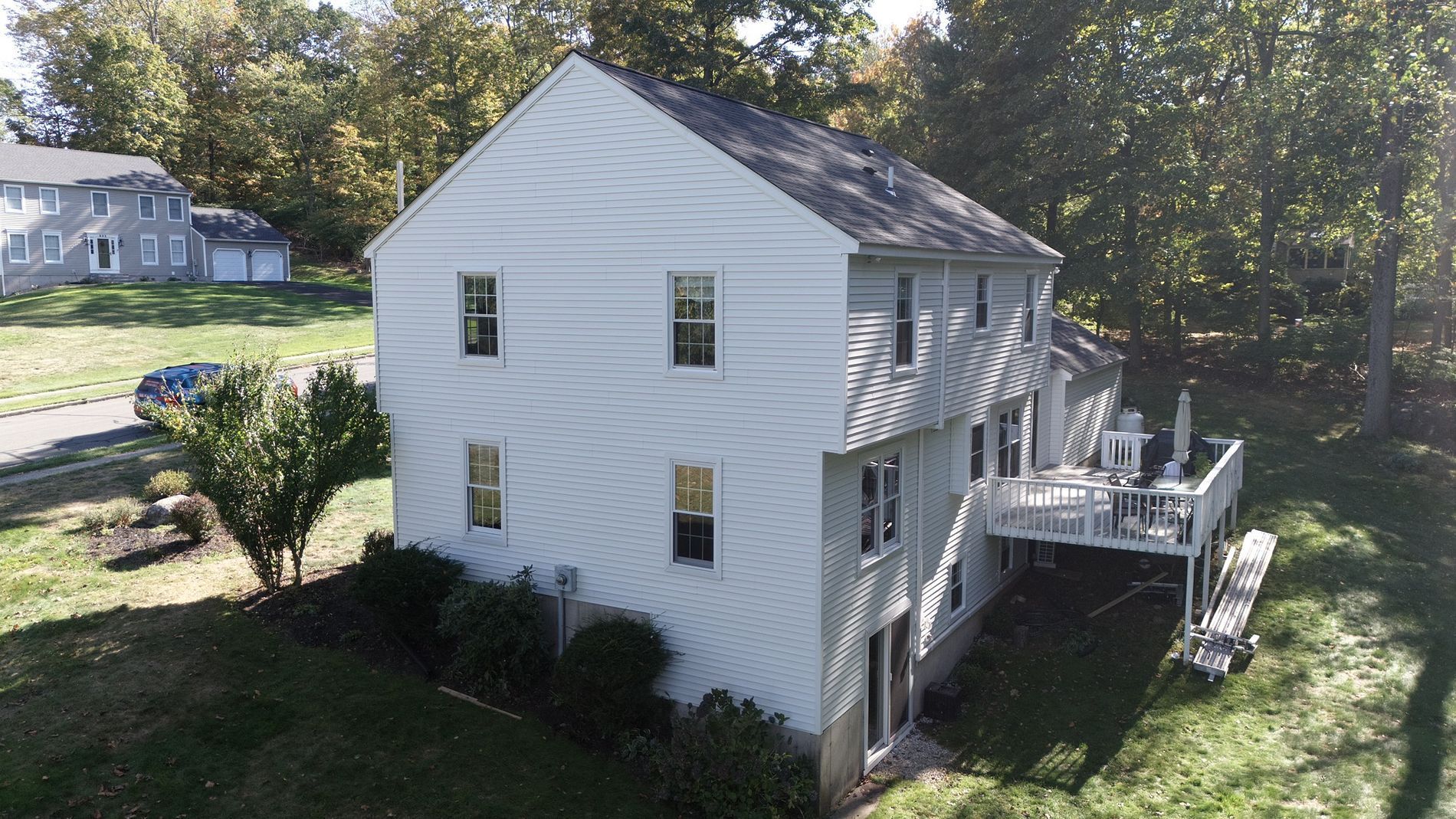 White two-story house with a side deck and stairs, surrounded by trees and grass.