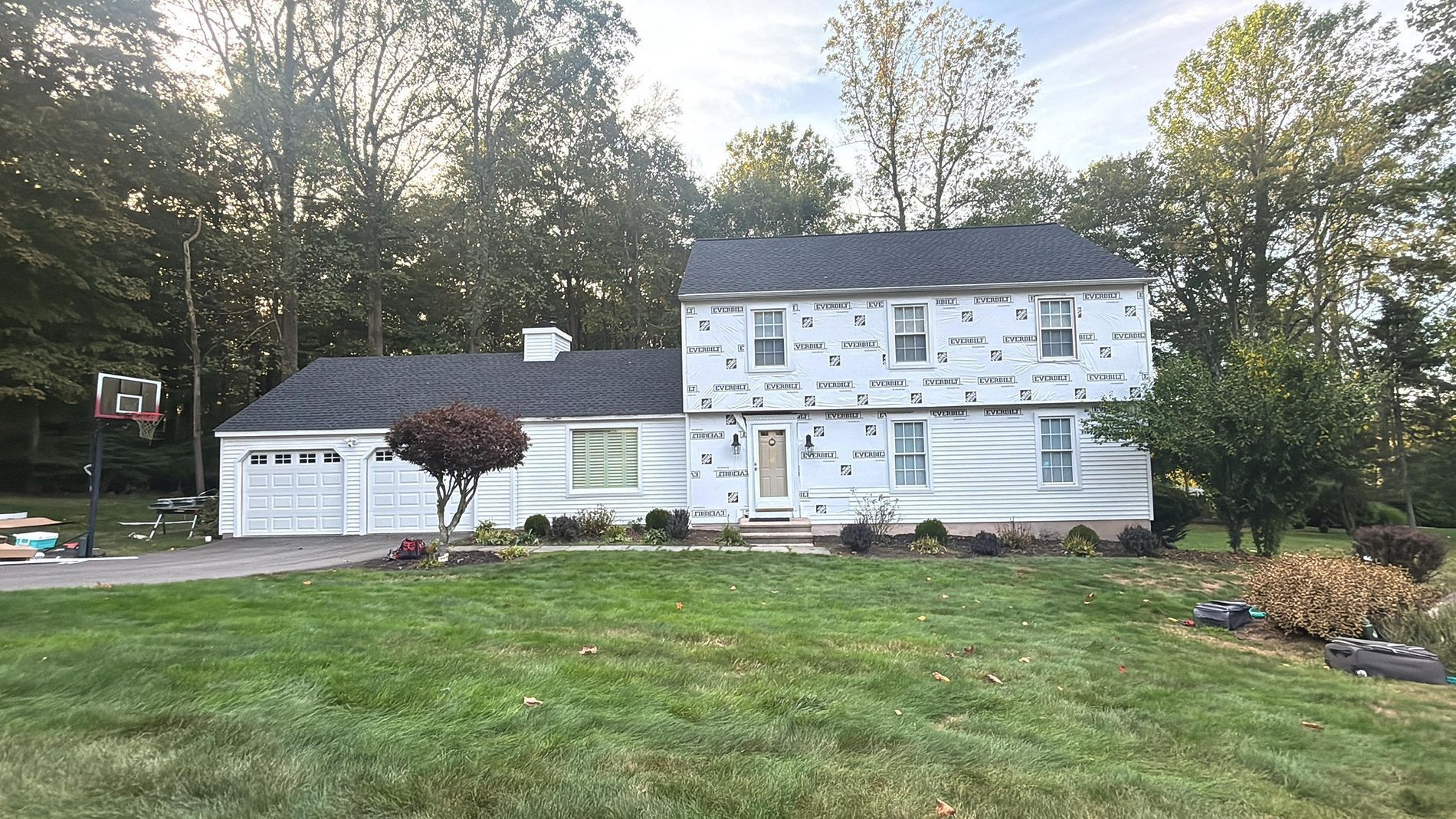 Suburban house under renovation with white house wrap and a wide green lawn in front