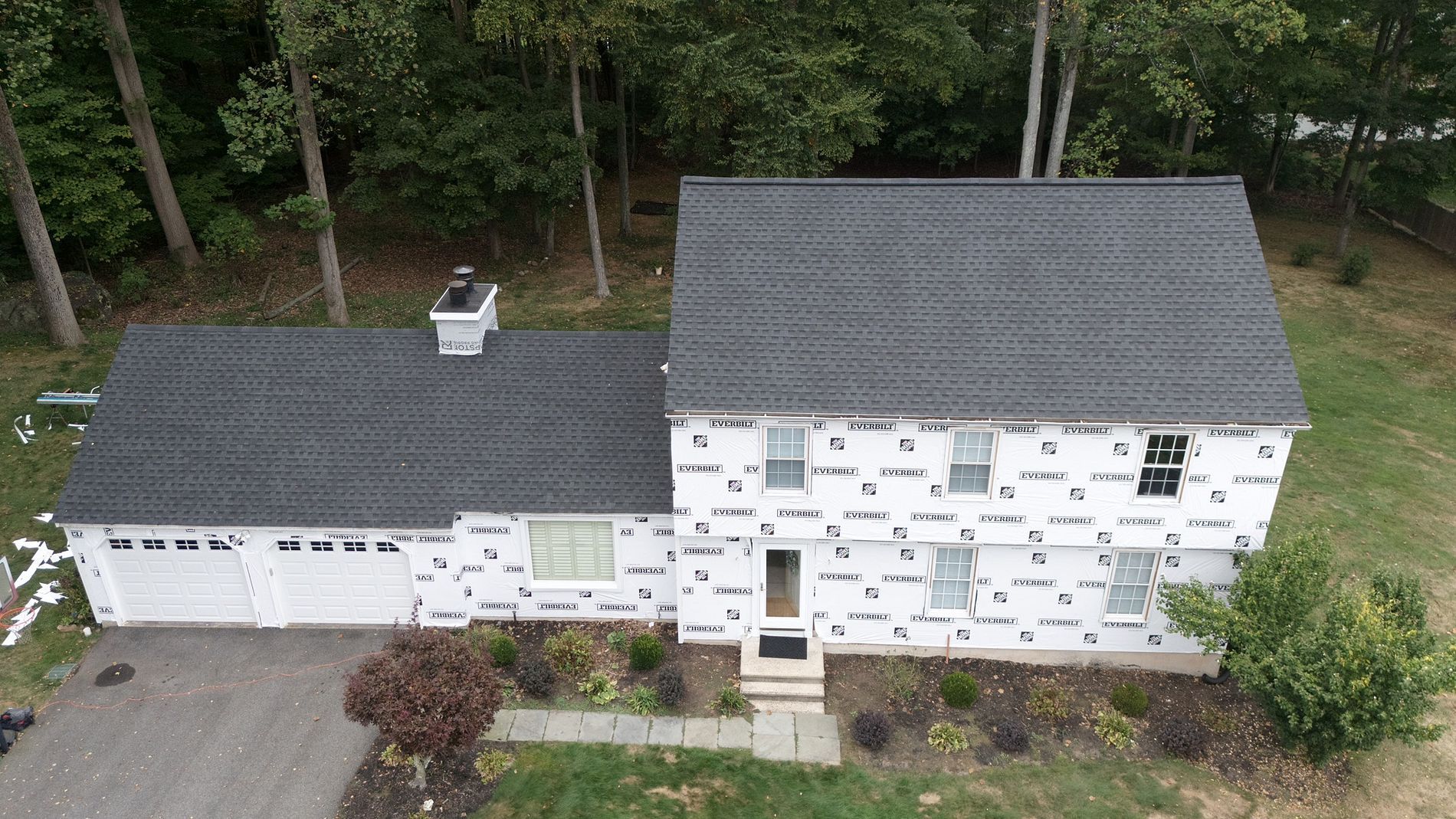 Aerial view of a white house with dark gray roof beside trees and a small front yard.