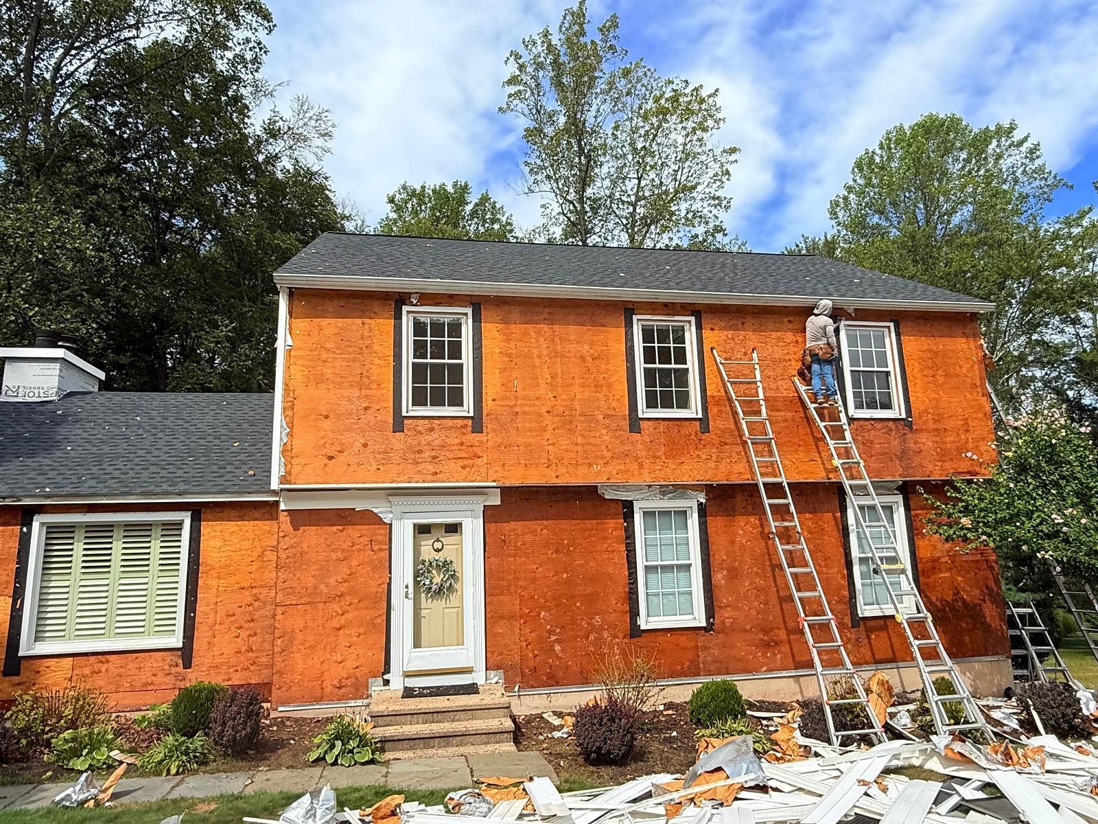 Orange house exterior with ladders leaning against the upper floor and roof under repair
