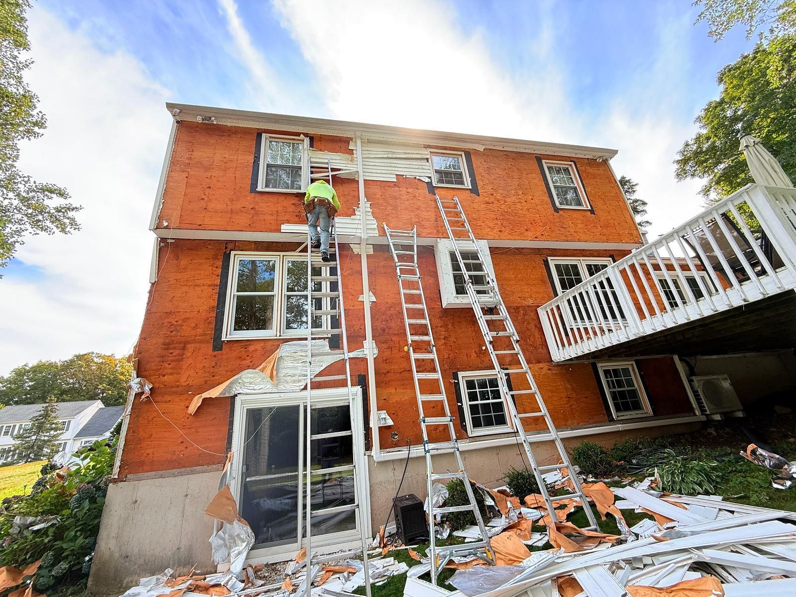 Worker on ladders outside an orange two-story house during exterior repairs.
