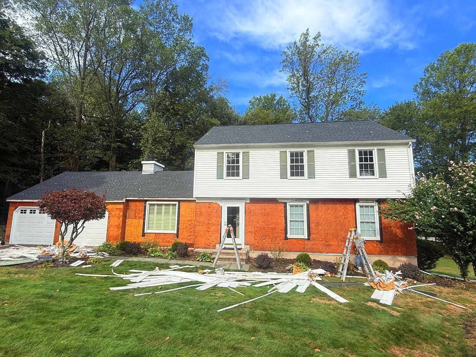 House under renovation with white upper story and orange lower walls, construction debris in front yard.