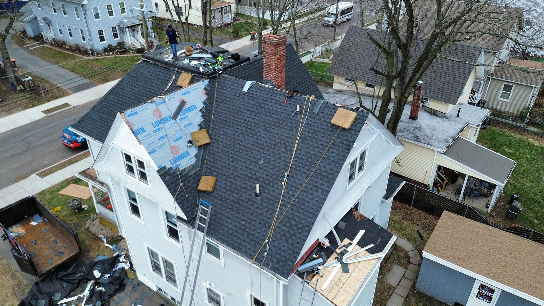 Drone view of a white house with a damaged roof under repair in a residential neighborhood
