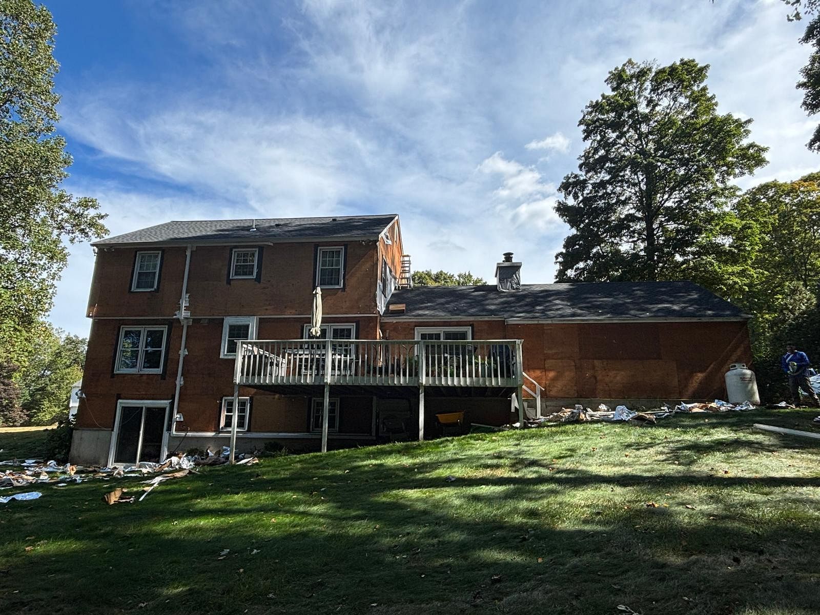 Brick house with a deck on a grassy slope under a partly cloudy sky