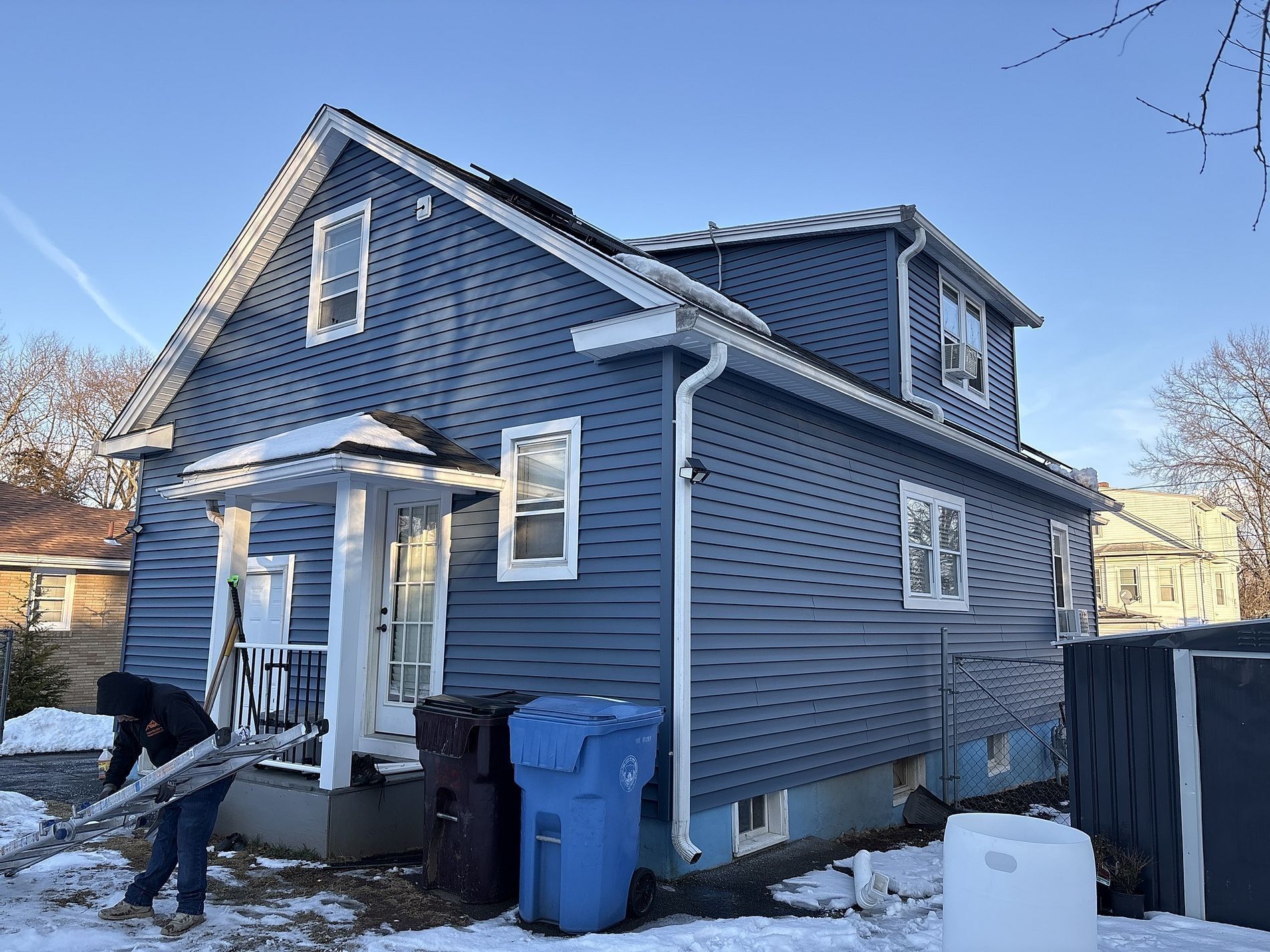 Blue two-story house with white trim and a person shoveling snow near the front steps