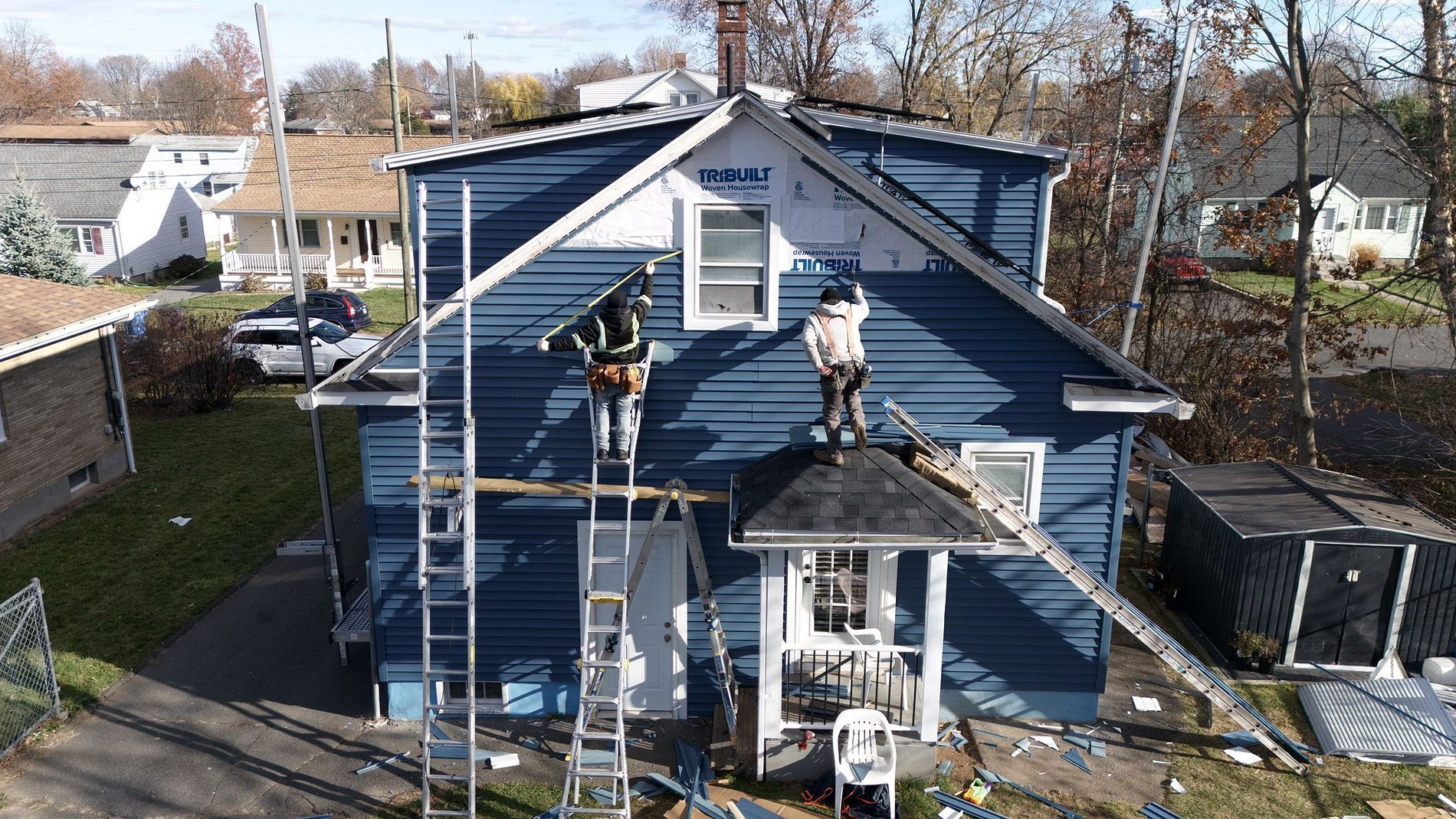 Two workers on ladders painting a blue house exterior with white trim.