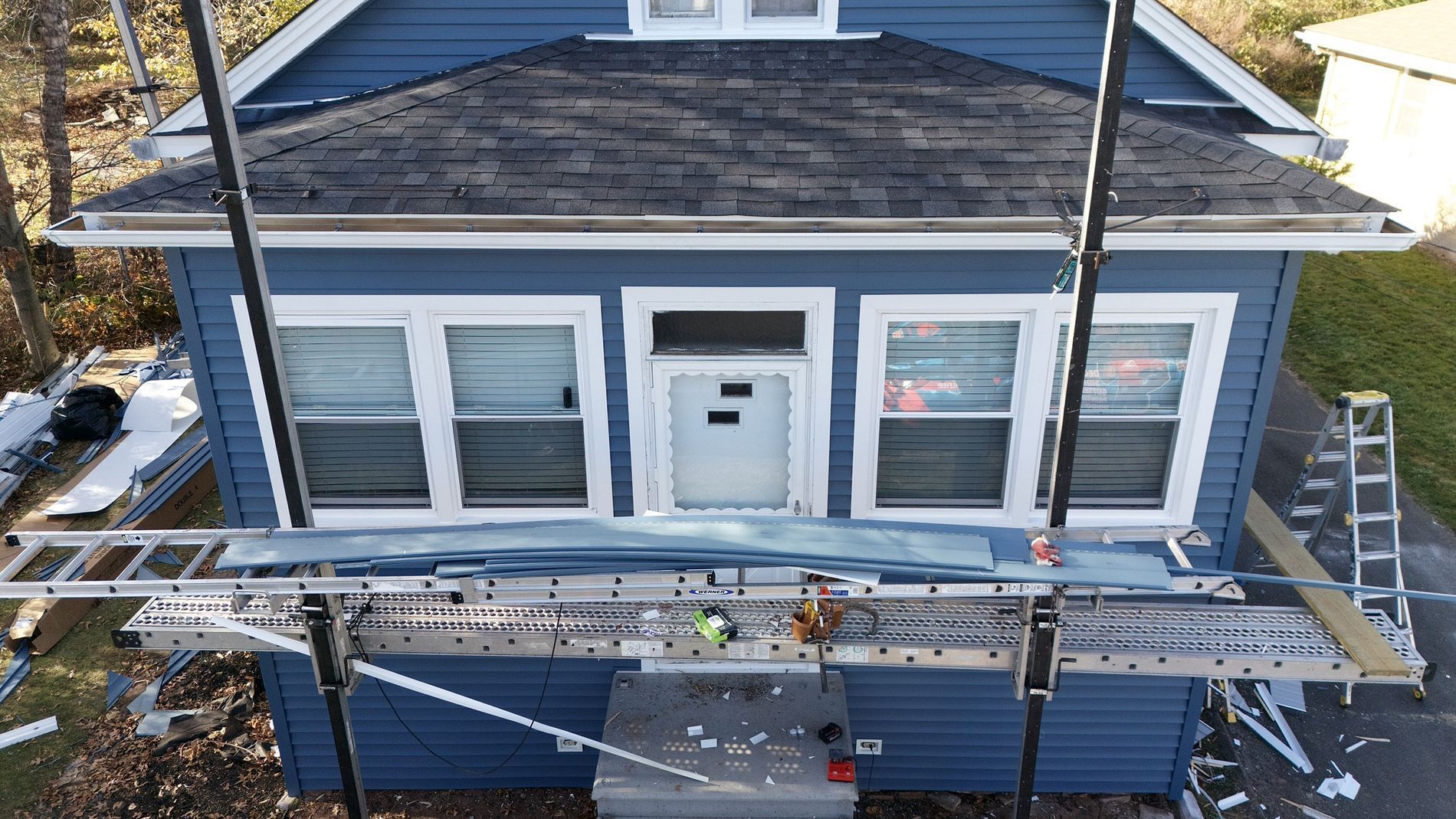 Workers on scaffolding repairing the blue exterior of a house with white trim and a central front door.