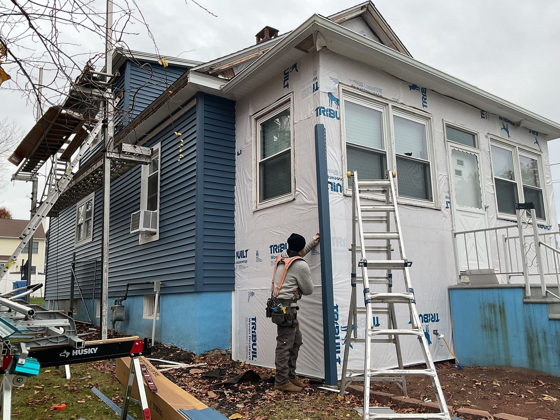 Person painting a blue house exterior beside a ladder and scattered tools