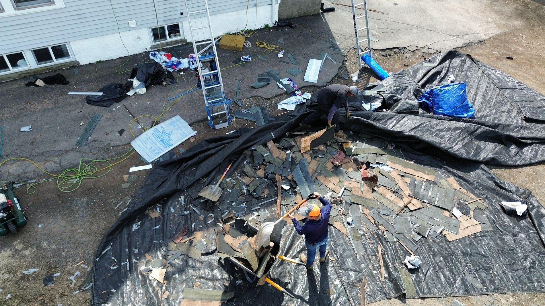 Roofing workers repairing a damaged roof with scattered debris and ladders nearby