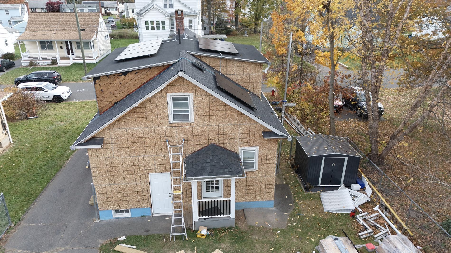 Aerial view of a brick house with a dark roof, front porch, and backyard shed in a leafy neighborhood
