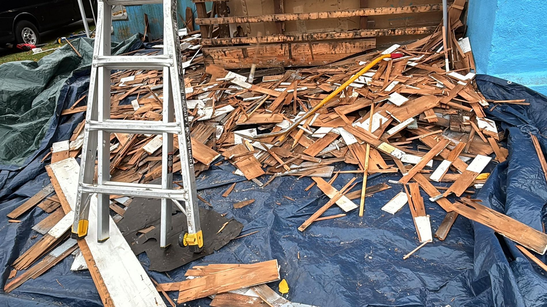 Damaged roof with a ladder and scattered broken wooden shingles on a blue tarp