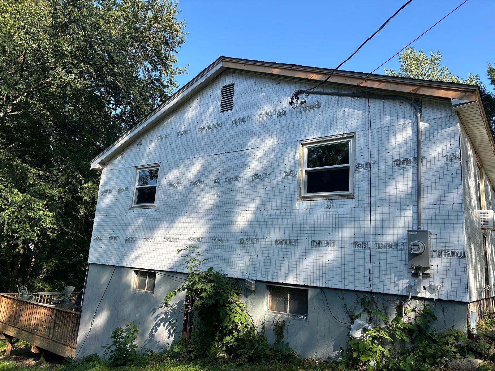 White house with peeling paint on a sloped, wooded hillside under bright daylight.