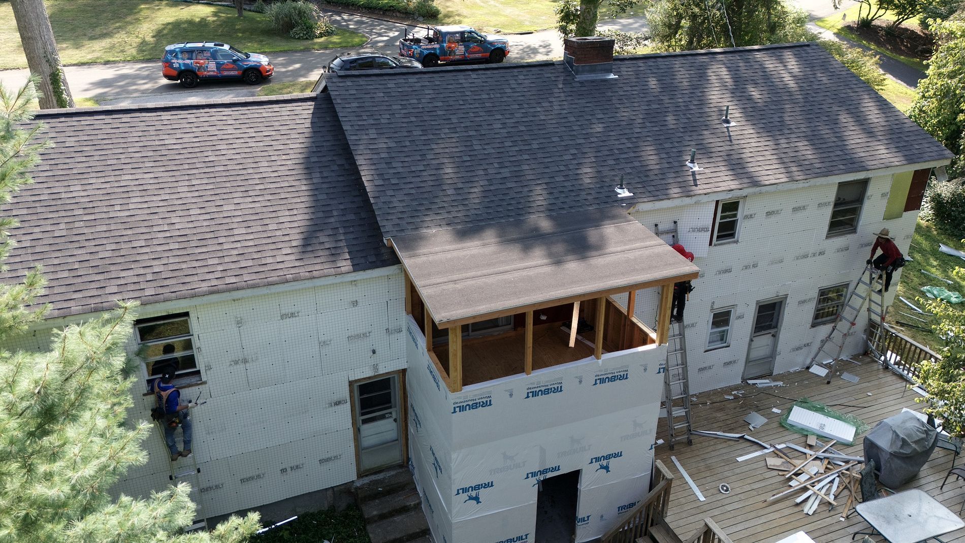 Aerial view of a house under renovation with a new roof, exposed framing, and construction materials below