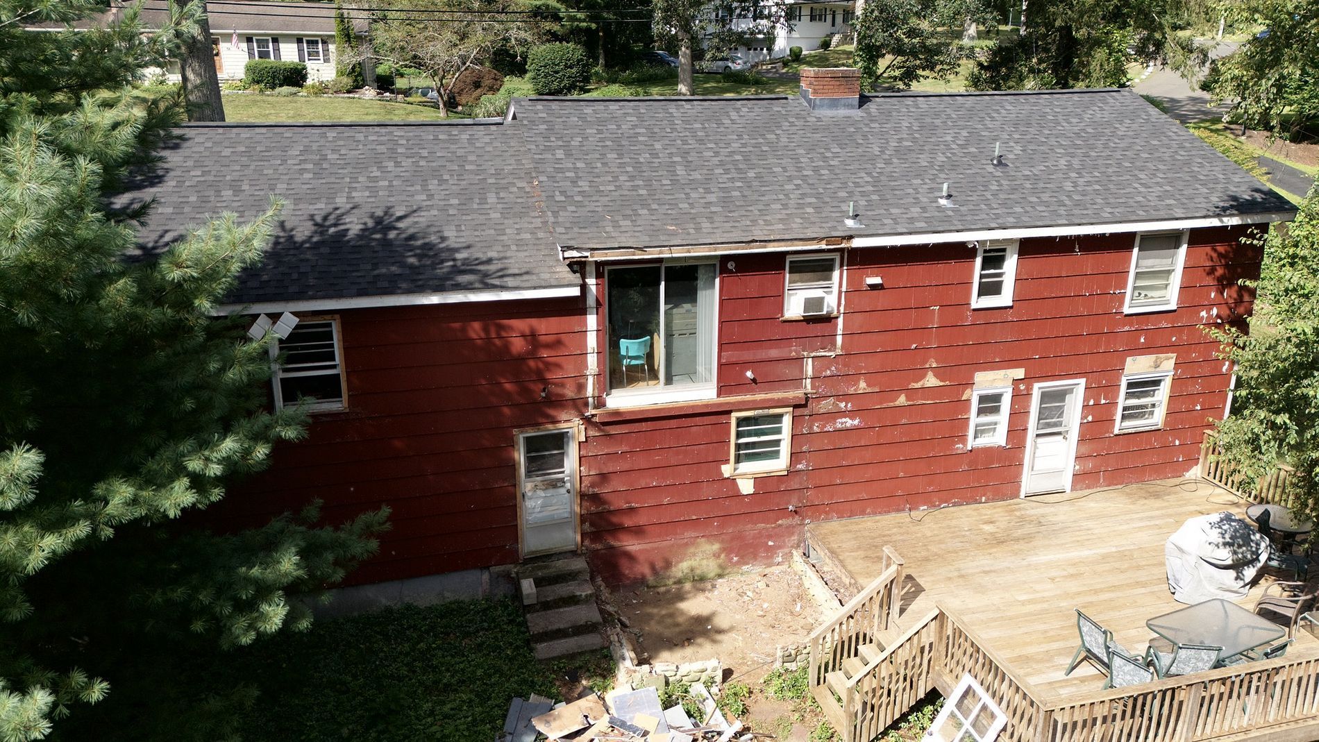 Red two-story house with a gray roof and a backyard deck under construction.