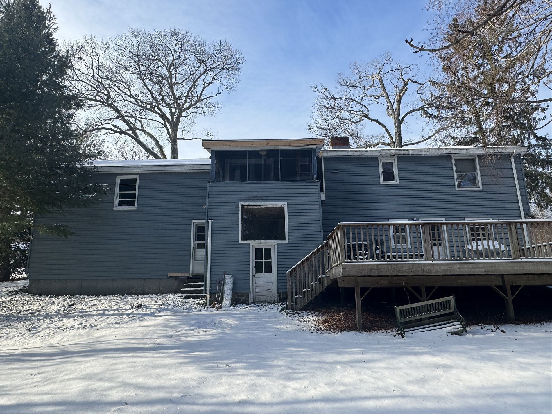 Snow-covered backyard with a gray two-story house and wooden deck under a clear winter sky
