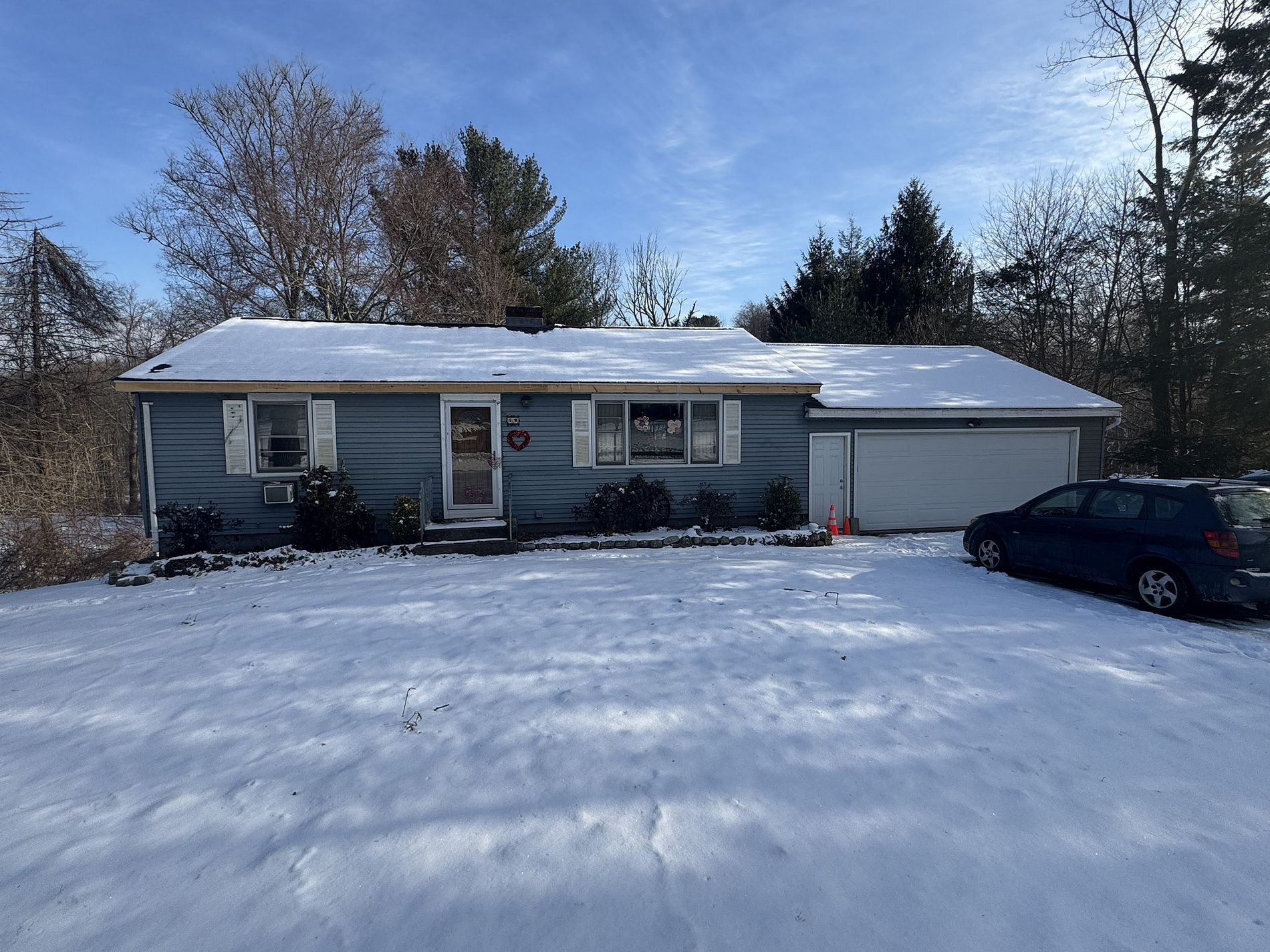 Snow-covered suburban house with a dark car parked in the driveway on a sunny winter day