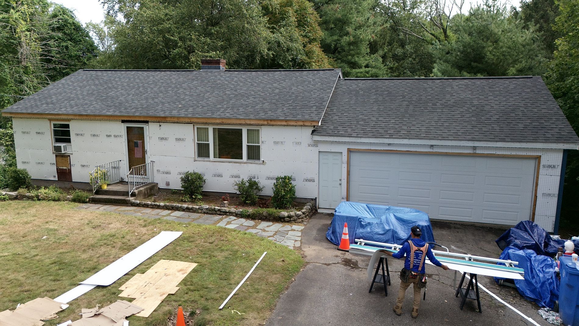 White single-story house with attached garage, front yard work materials, and two dirt bikes in the driveway