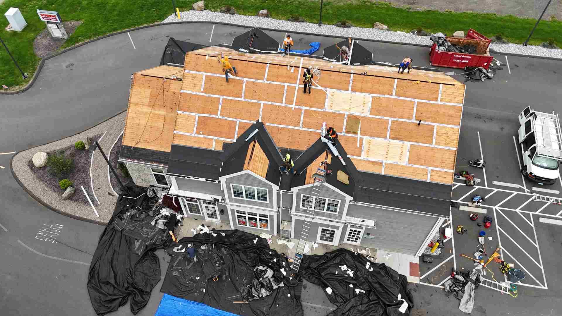 Aerial view of a house with severe roof damage and orange tarps, with debris and emergency vehicles nearby.