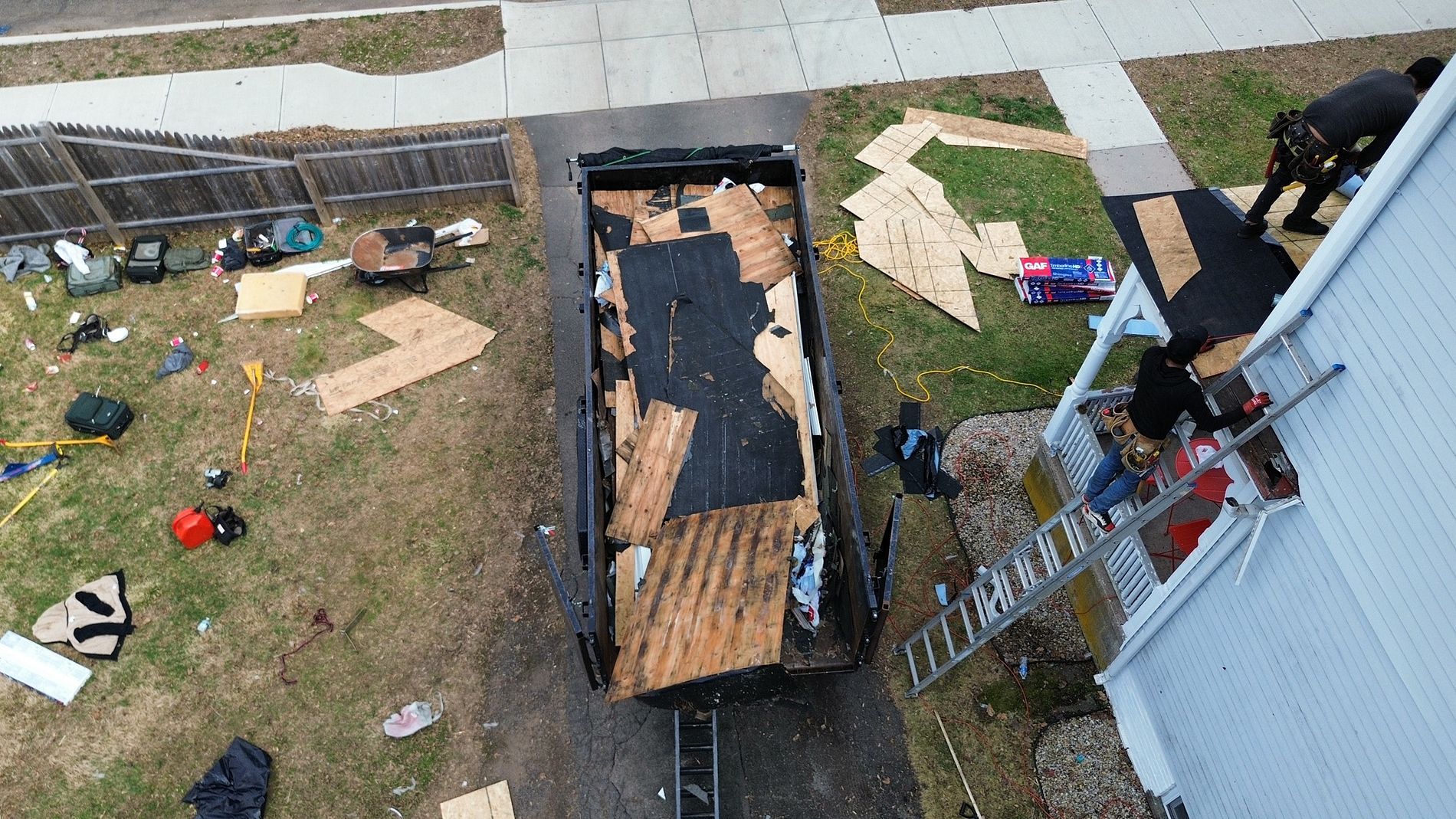 Aerial view of a backyard with a charred, damaged trailer beside a house and scattered debris.