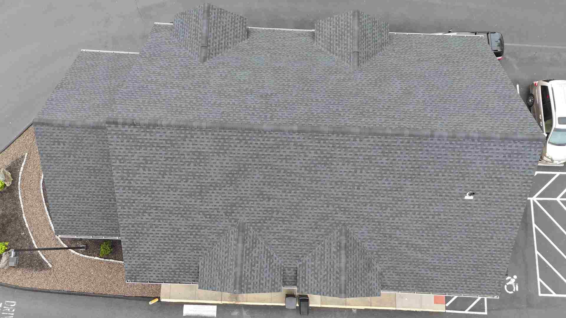 Aerial view of a gray shingled house roof with chimneys and a driveway on the left.