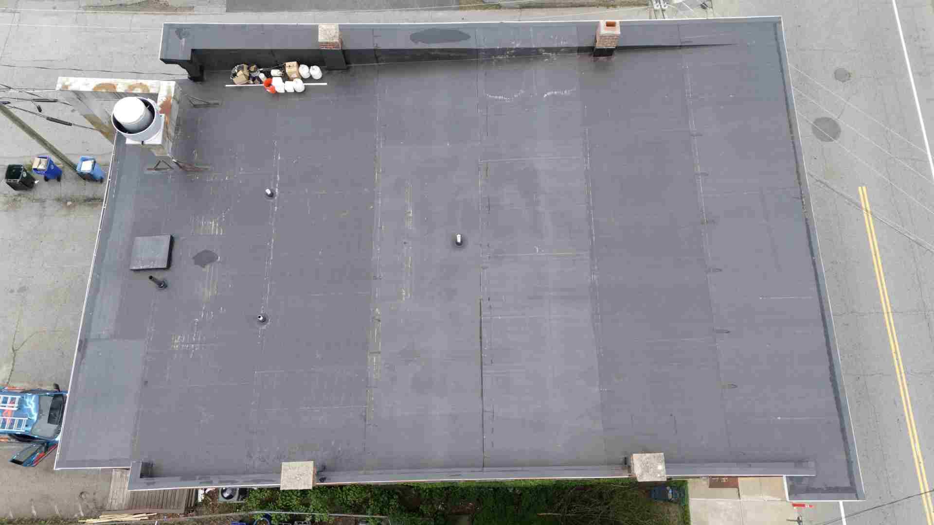 Aerial view of a flat gray roof with vents, HVAC units, and utility equipment around the edges