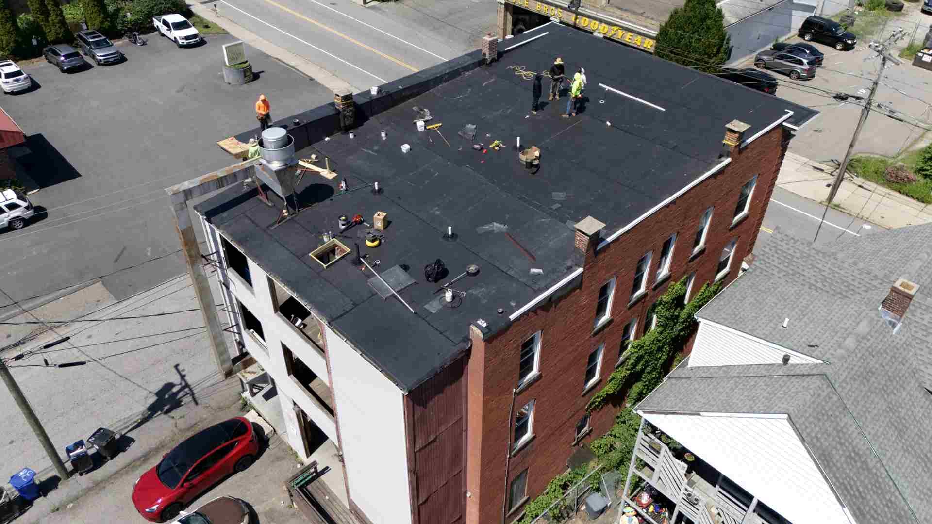 Aerial view of workers on a flat-roofed brick building in an urban street scene