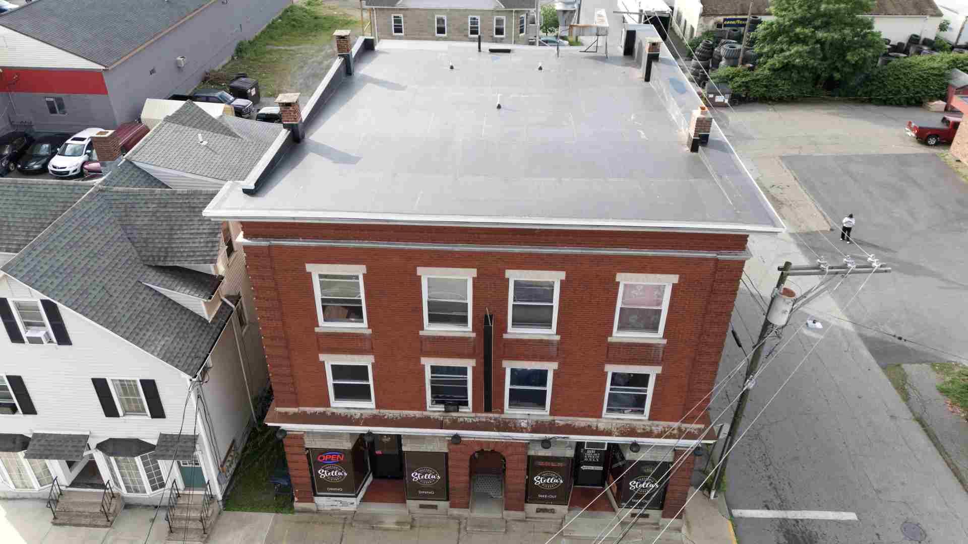 Aerial view of a red brick three-story building with storefronts on a street corner.