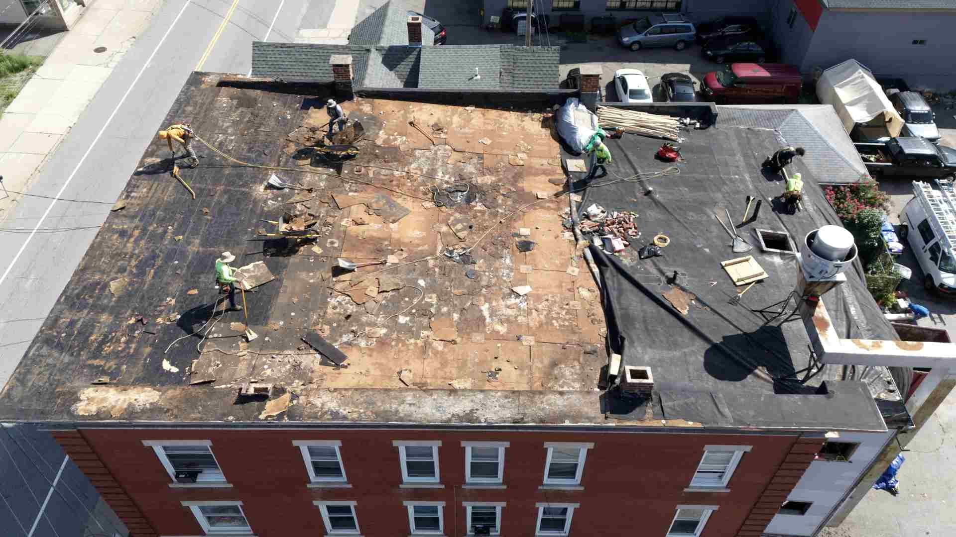 Aerial view of a damaged flat roof with debris and workers repairing it on a red brick building.
