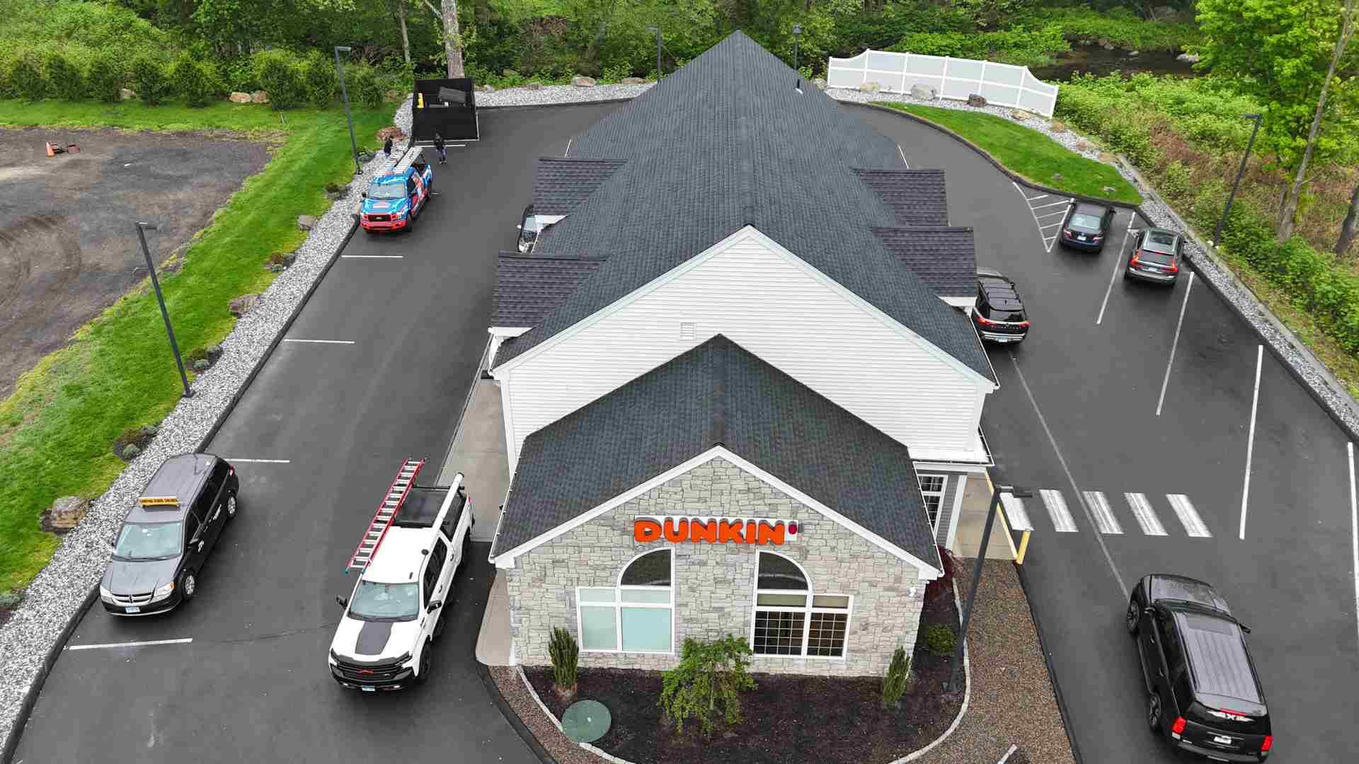 Aerial view of a small building with parked cars in a lot, surrounded by greenery.