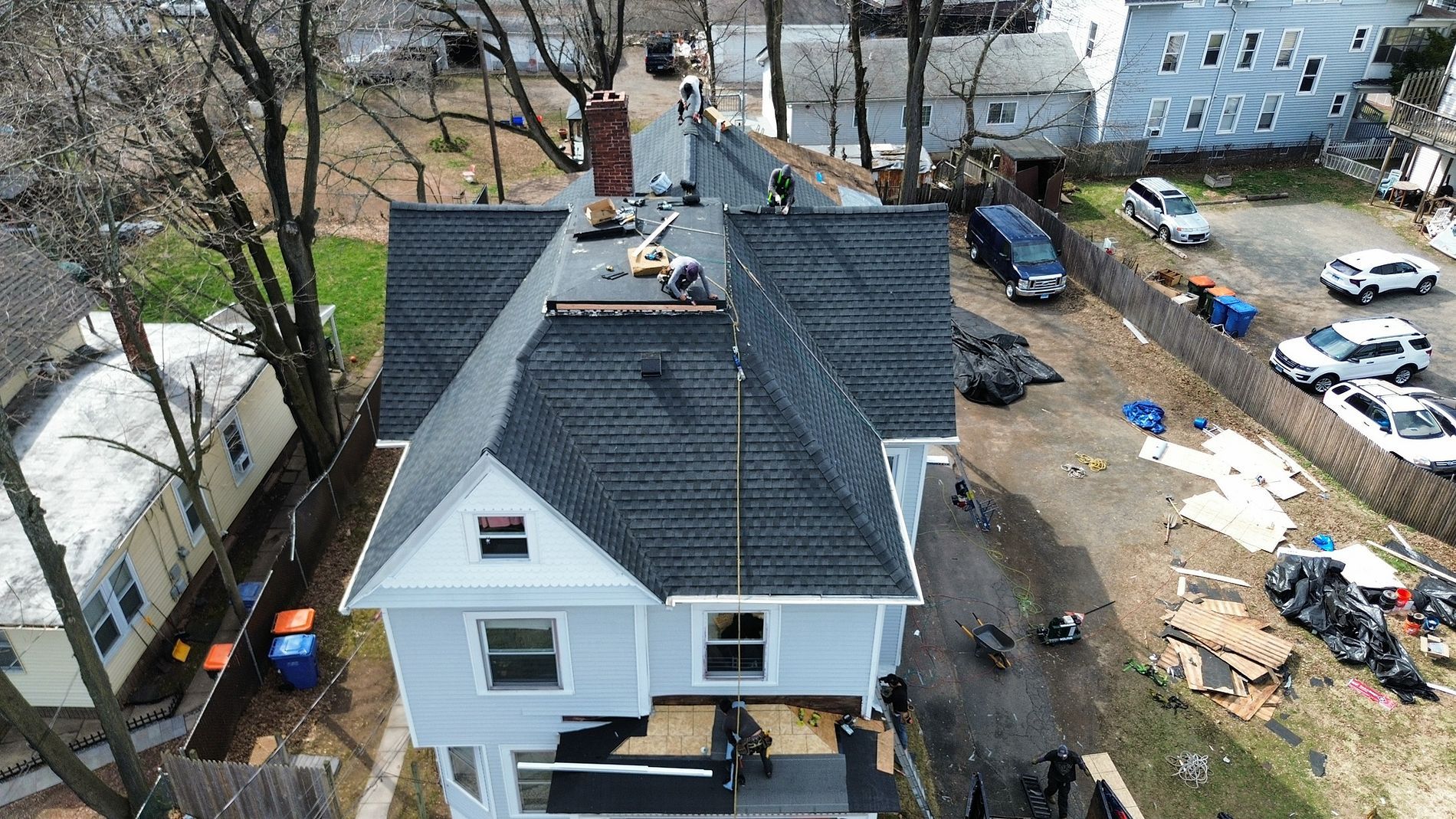 Aerial view of a white house with a dark roof beside a driveway and construction debris in the yard
