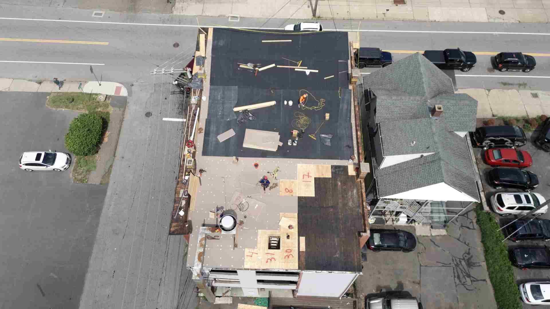 Aerial view of a residential street with houses, parked cars, and a roof under repair.