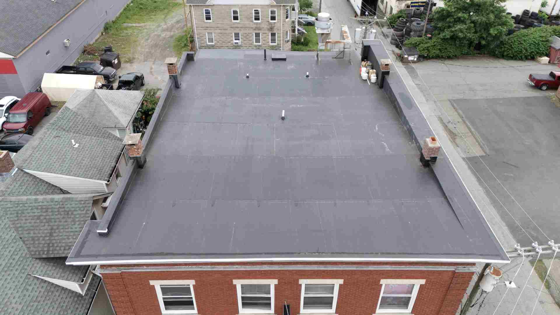Aerial view of a flat rooftop with HVAC units and neighboring brick buildings.