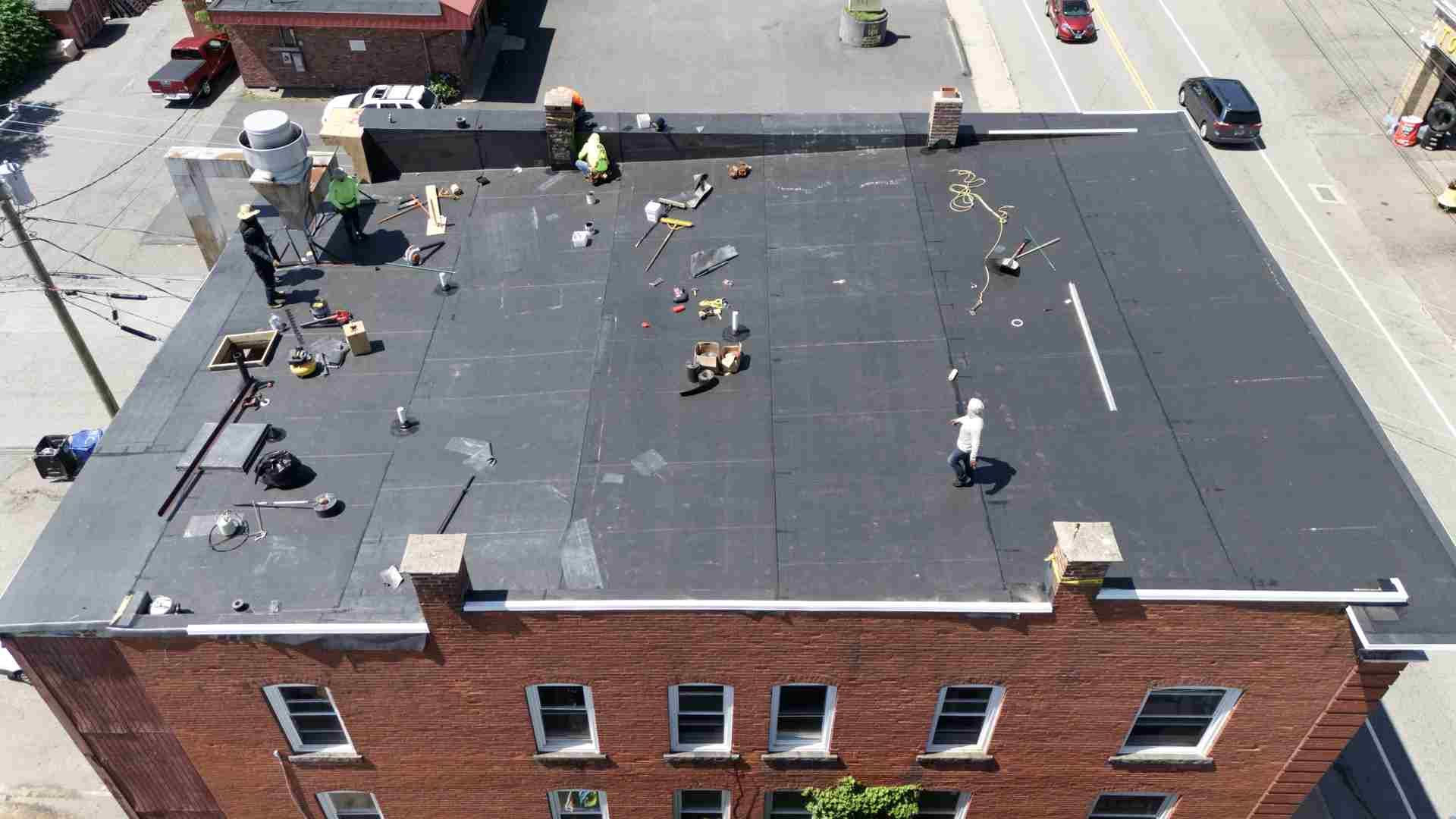 Aerial view of workers on a flat rooftop beside a street and brick building.