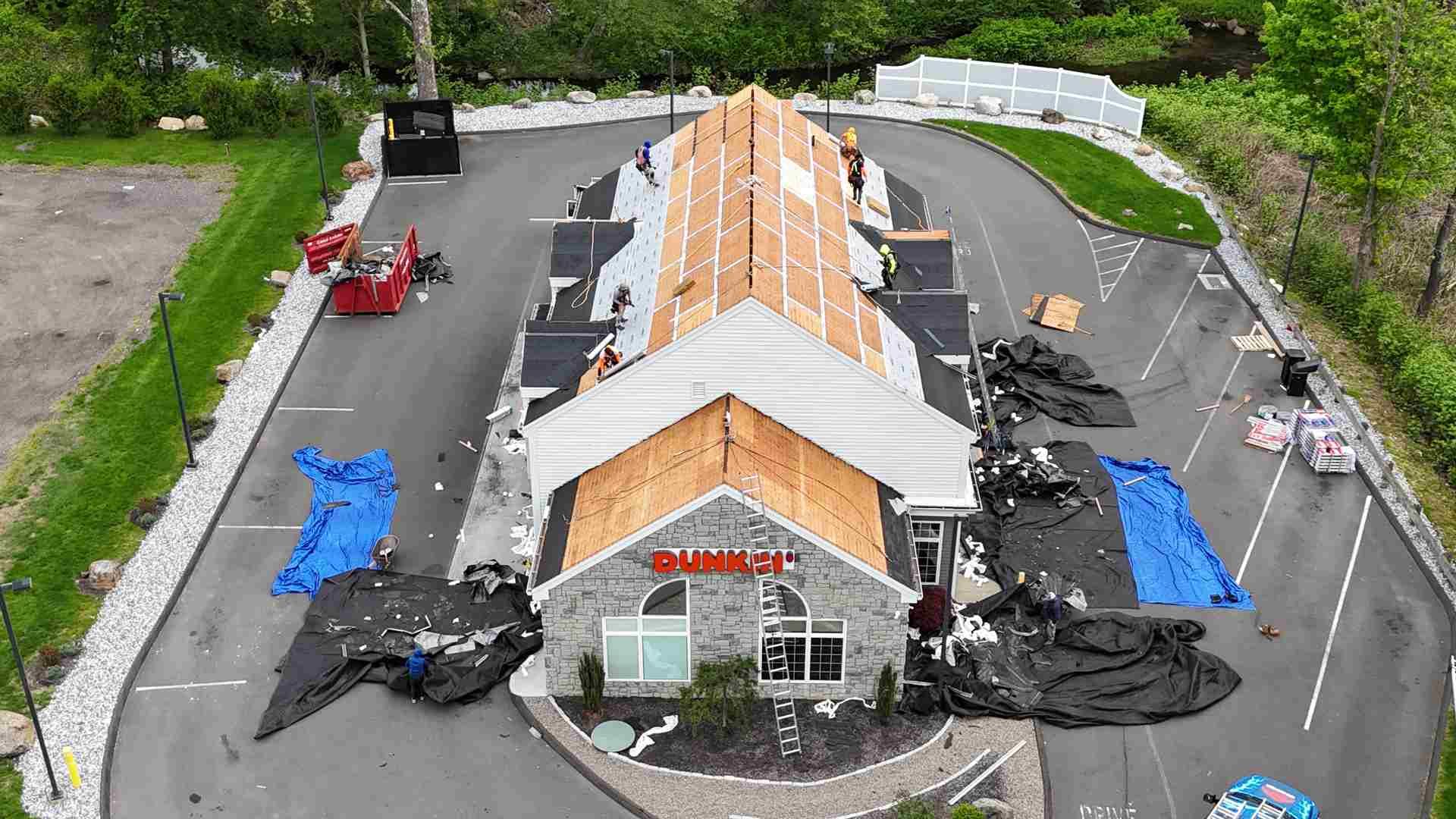 Aerial view of a building under construction with orange roofing, black tarps, and surrounding materials