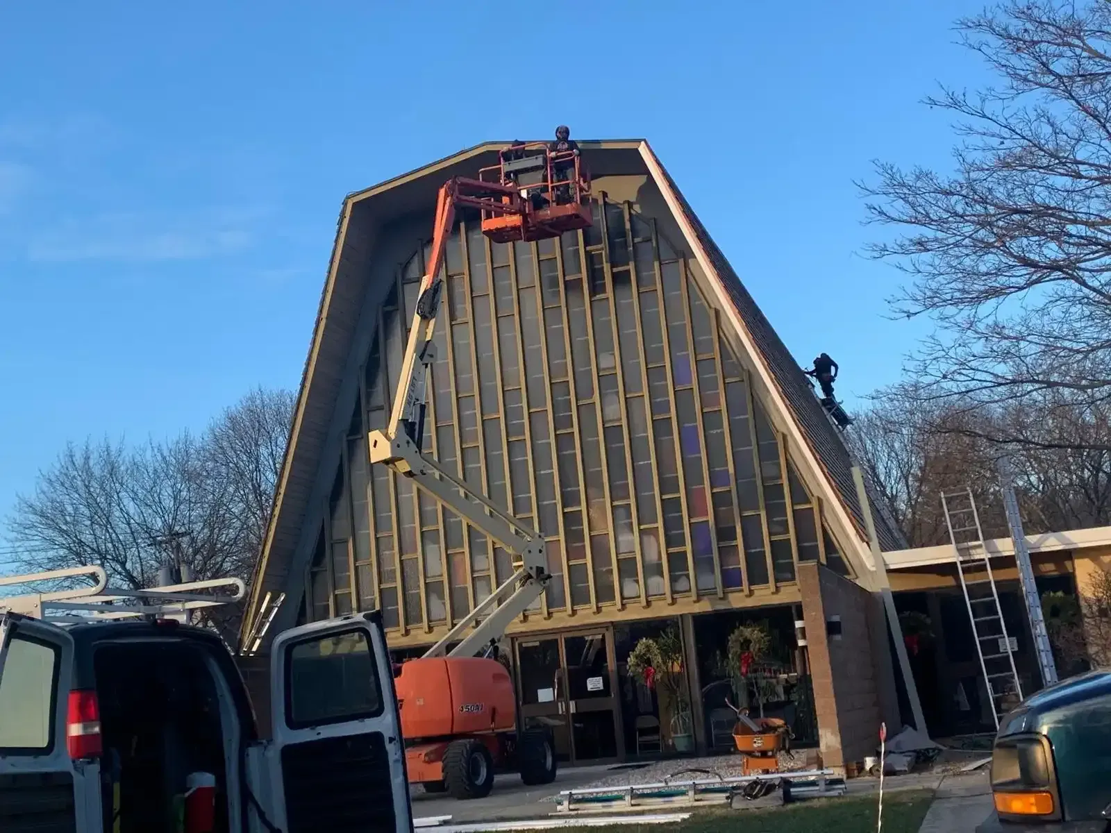Barn with a steep roof under repair, with construction lift and vehicles in front.